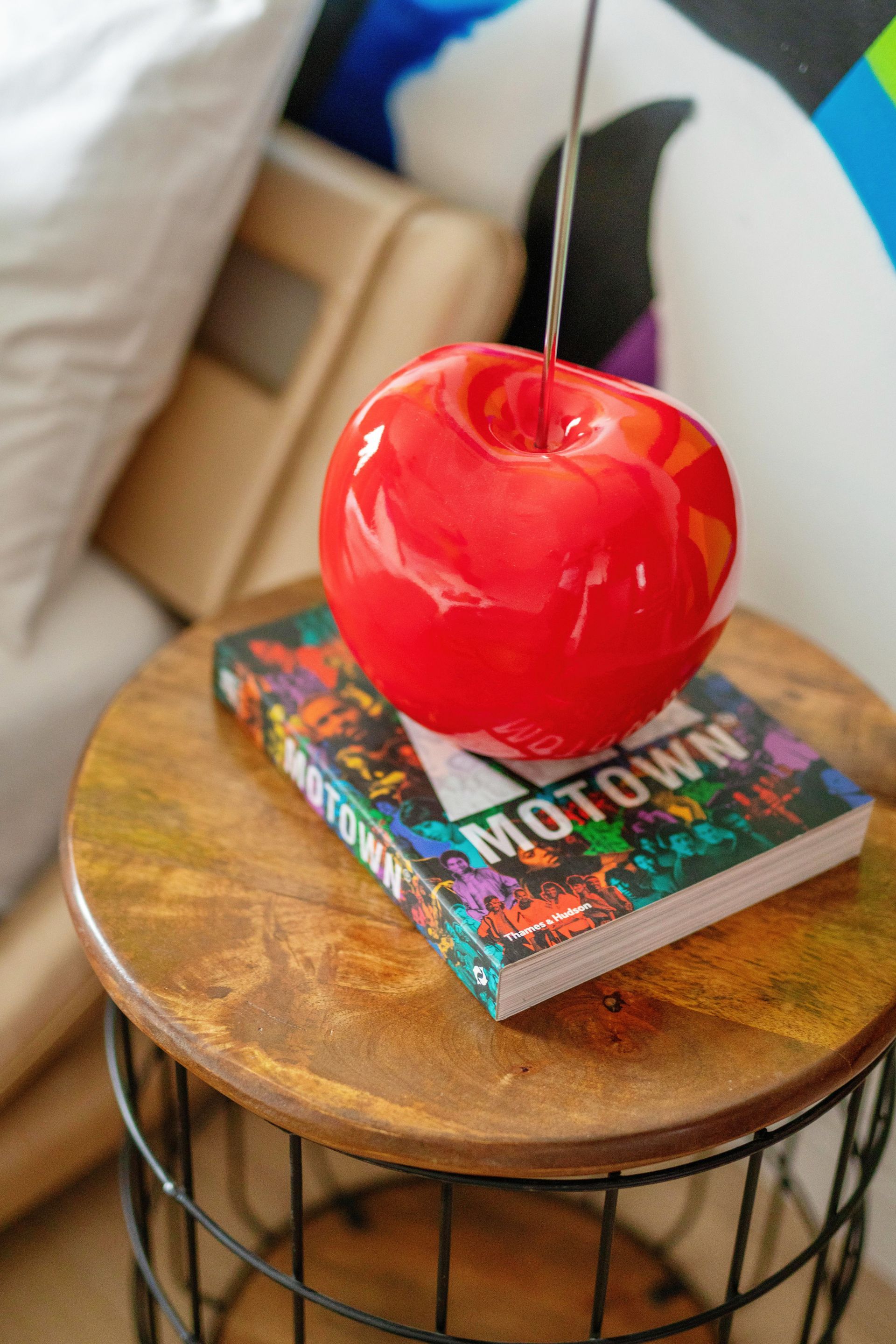Red candy apple on a colorful book atop a round wooden table next to a wire basket