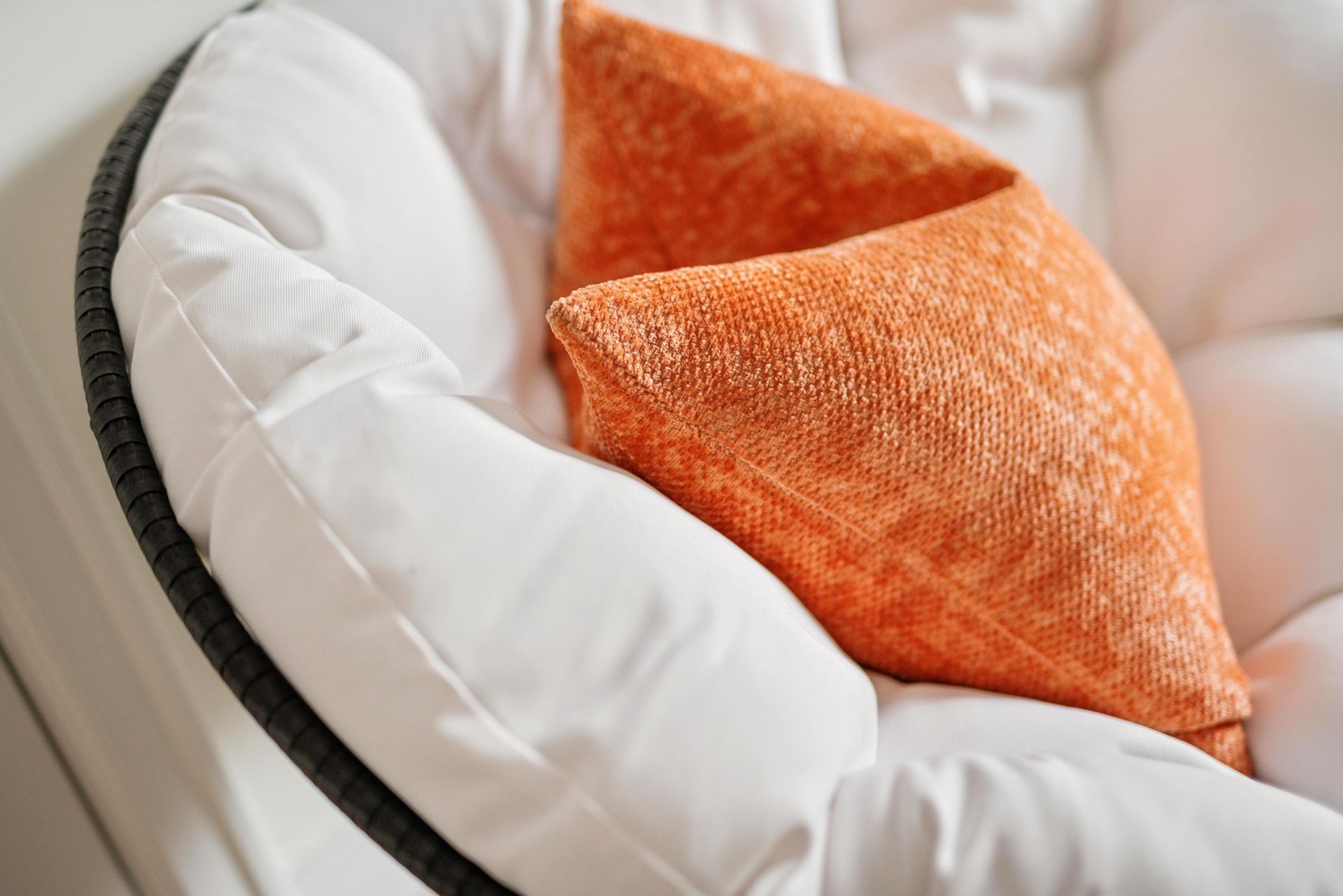 White cushioned chair with a textured orange pillow