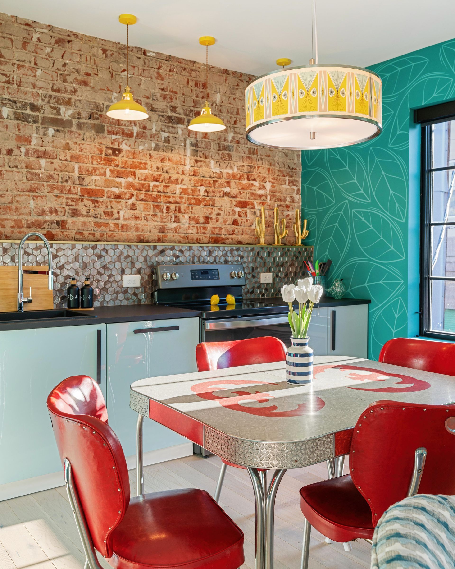 Bright kitchen with red chairs, brick wall, teal accent wall, and pendant lights around a dining table