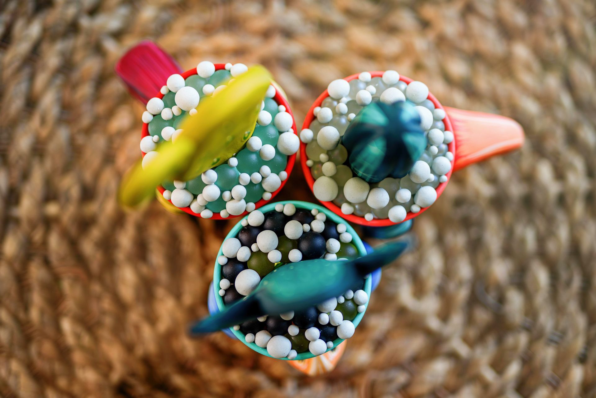 Three colorful beaded spinning tops on a woven straw surface.