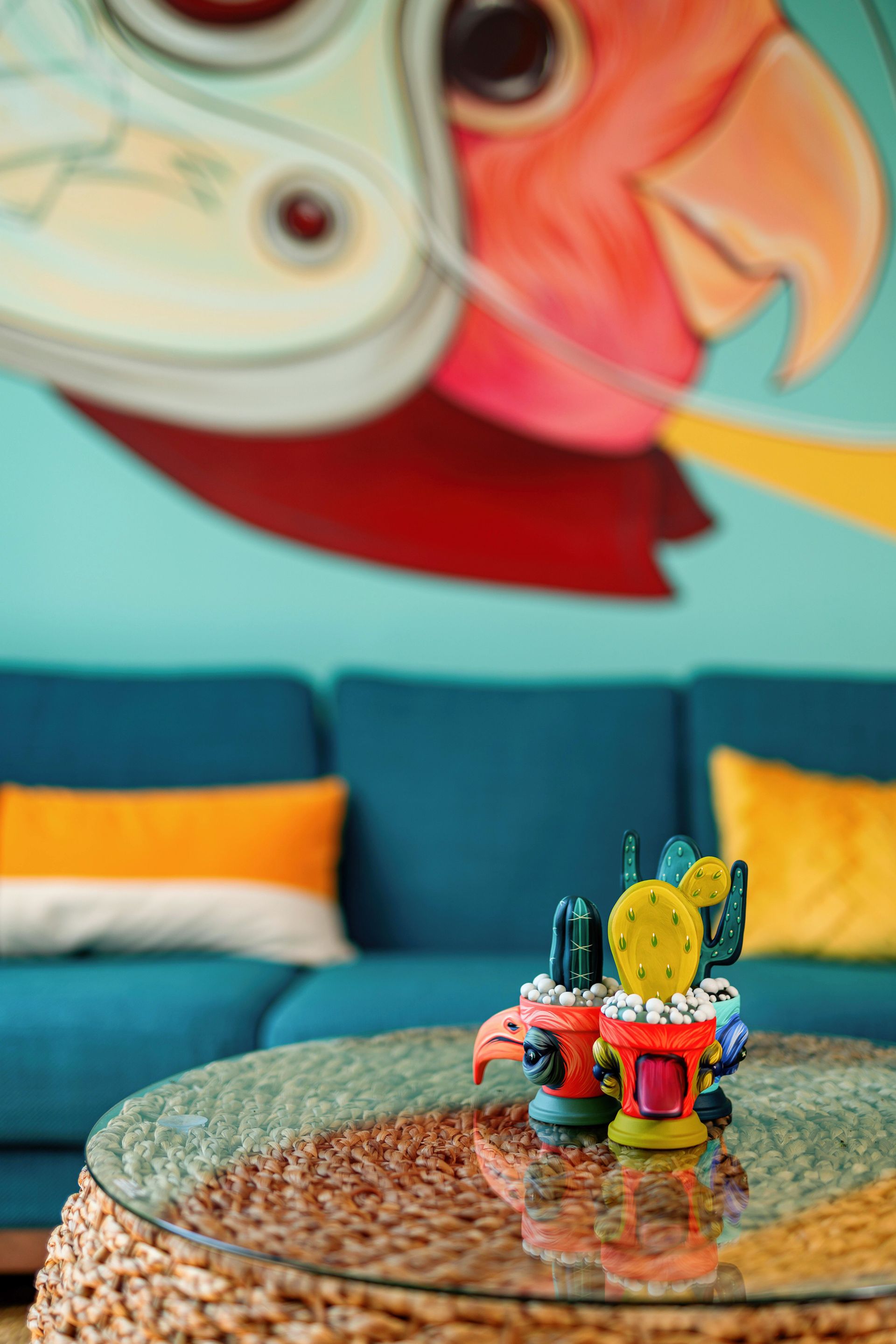 Small figurines on a round glass table in a teal living room beneath a colorful mural.