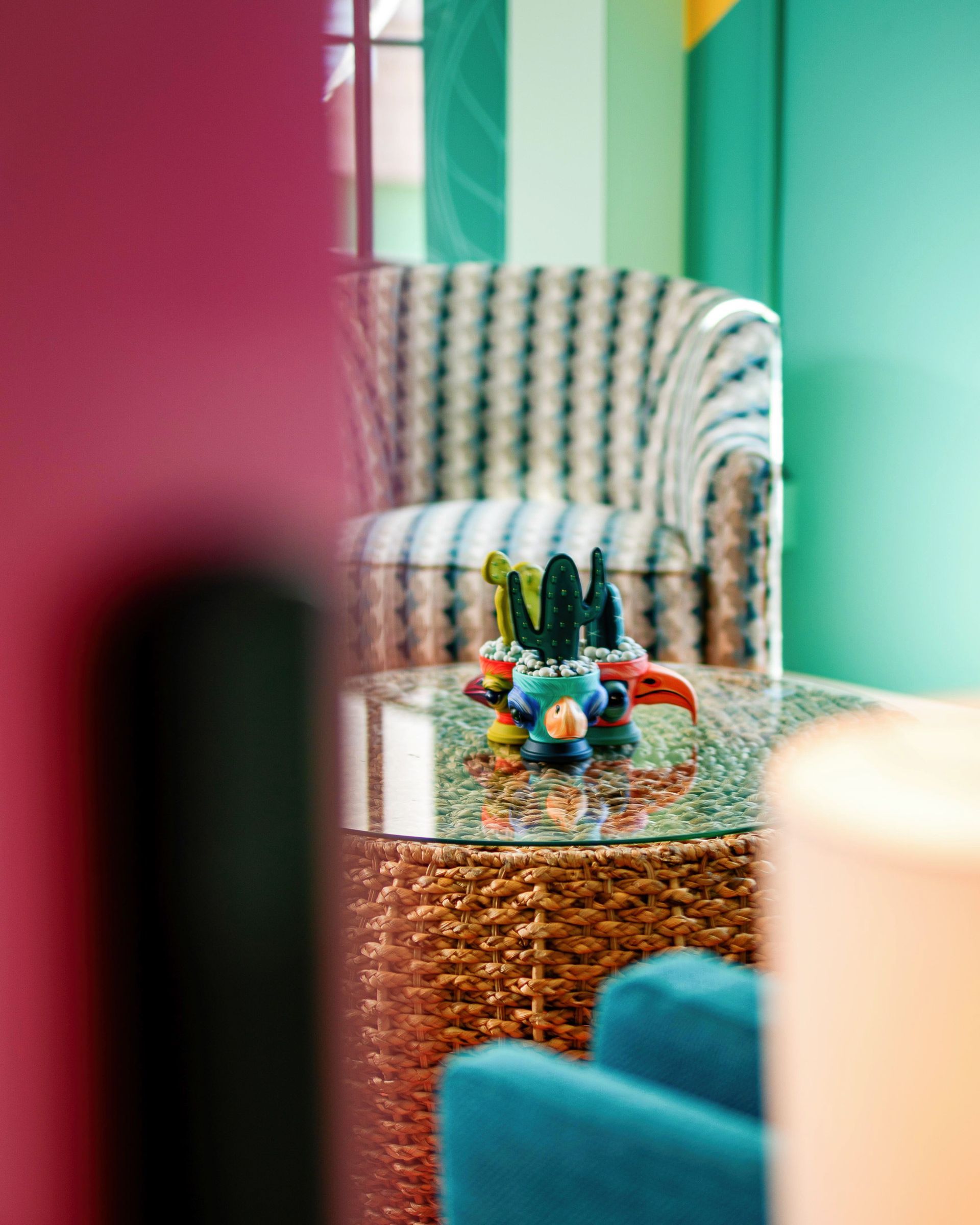 Small wicker table with colorful figurines between teal chairs in a bright lounge area