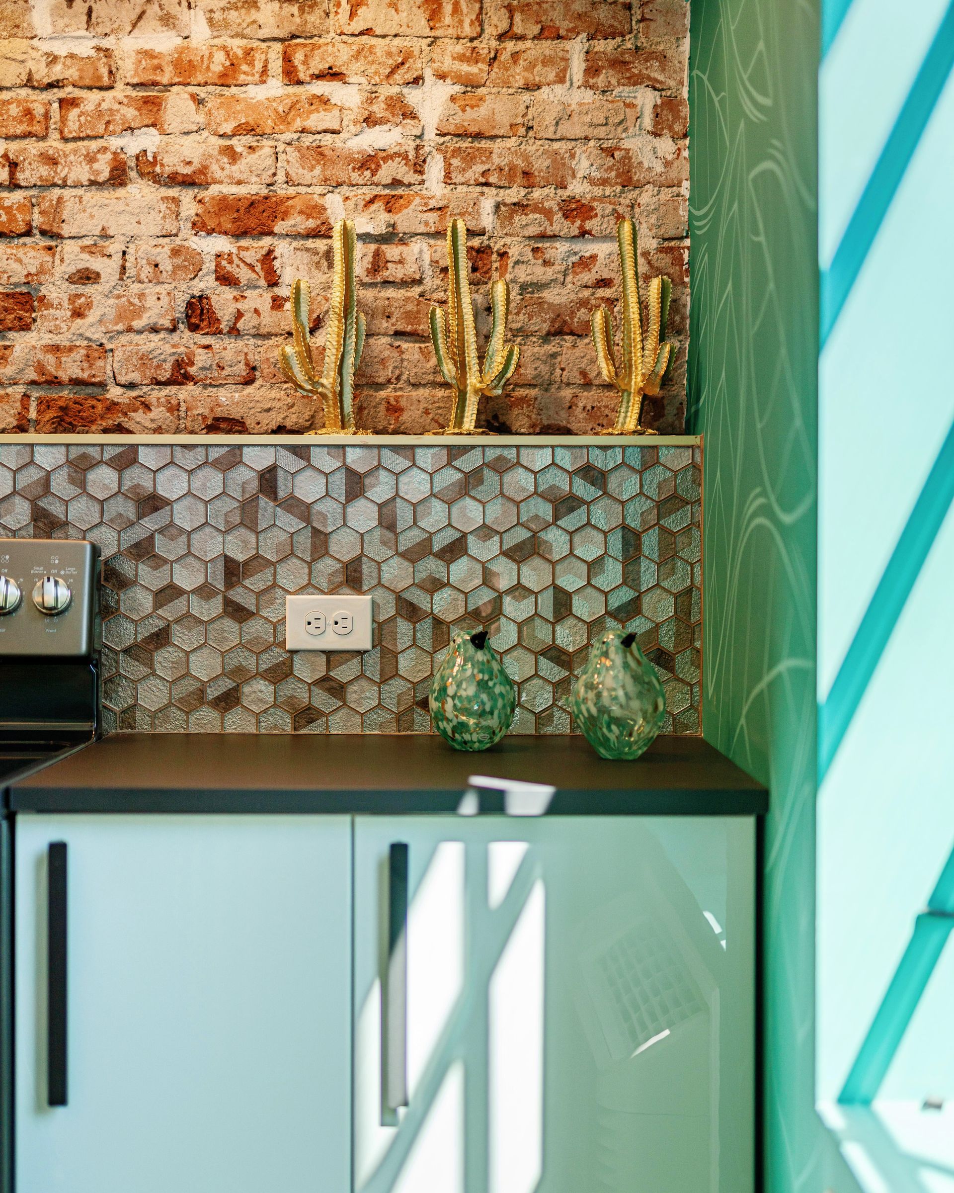 Modern kitchen corner with brick wall, teal cabinets, and turquoise patterned accent wall.