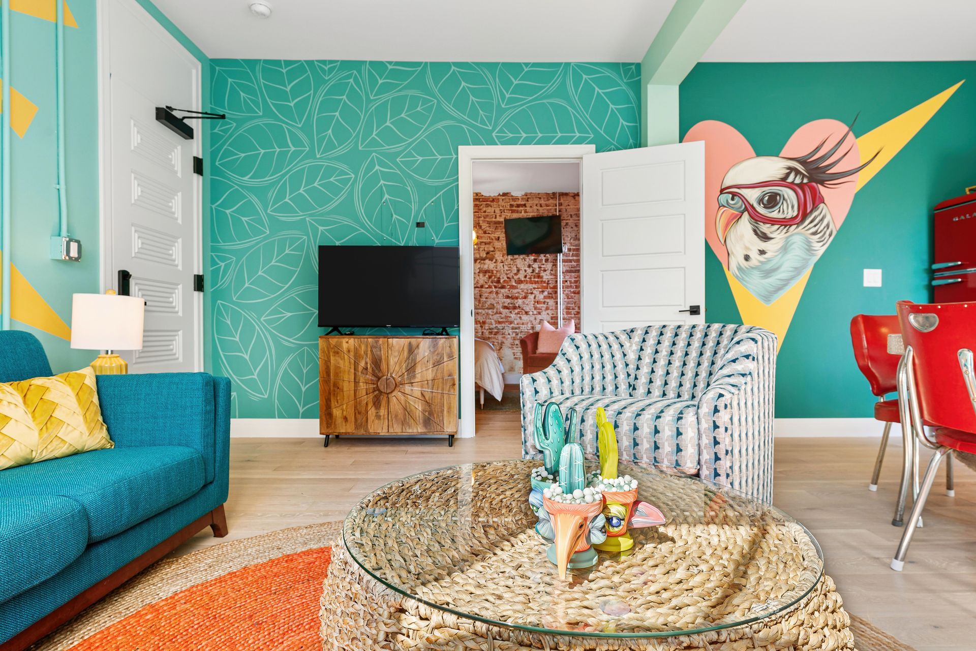 Bright teal living room with patterned walls, cozy sofa, TV, rattan coffee table, and colorful wall art