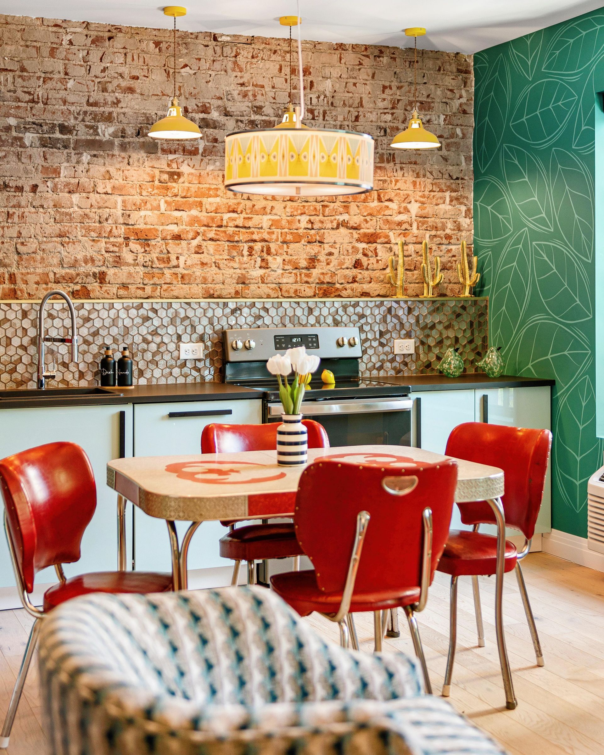 Cozy dining area with red chairs, round table, brick wall, green accent wall, and pendant lights