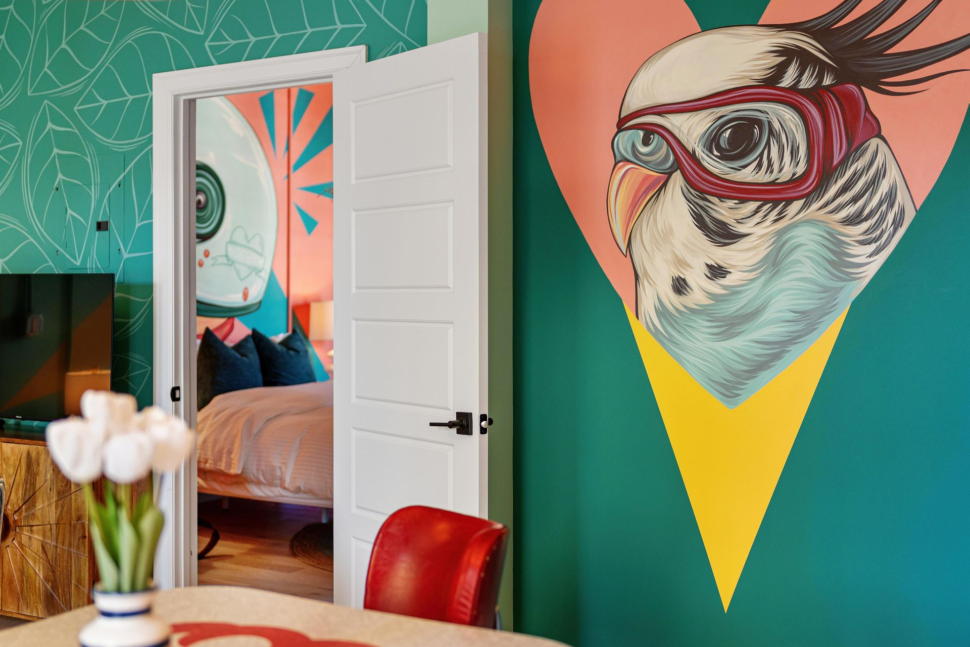 Colorful modern room with an open door, teal wall, and a large mural of a bird wearing goggles.