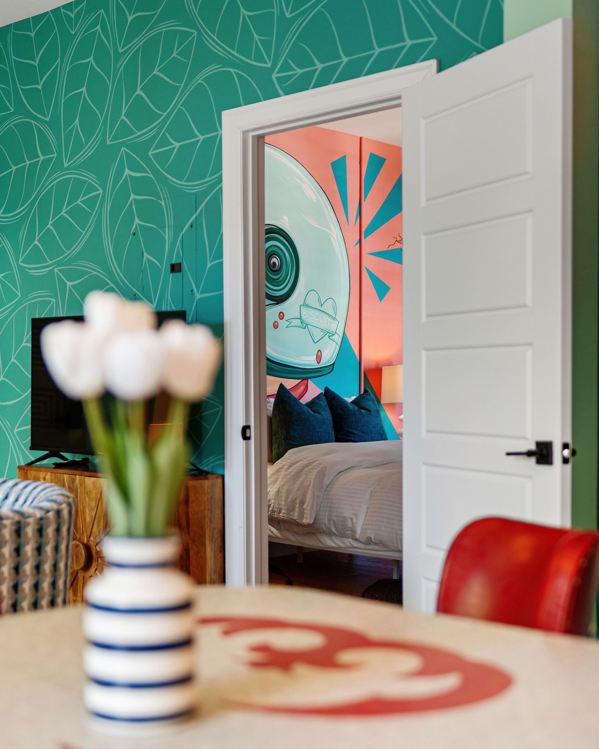 Bright room with teal patterned wall, open white door, and blurred tulips on a table in the foreground.