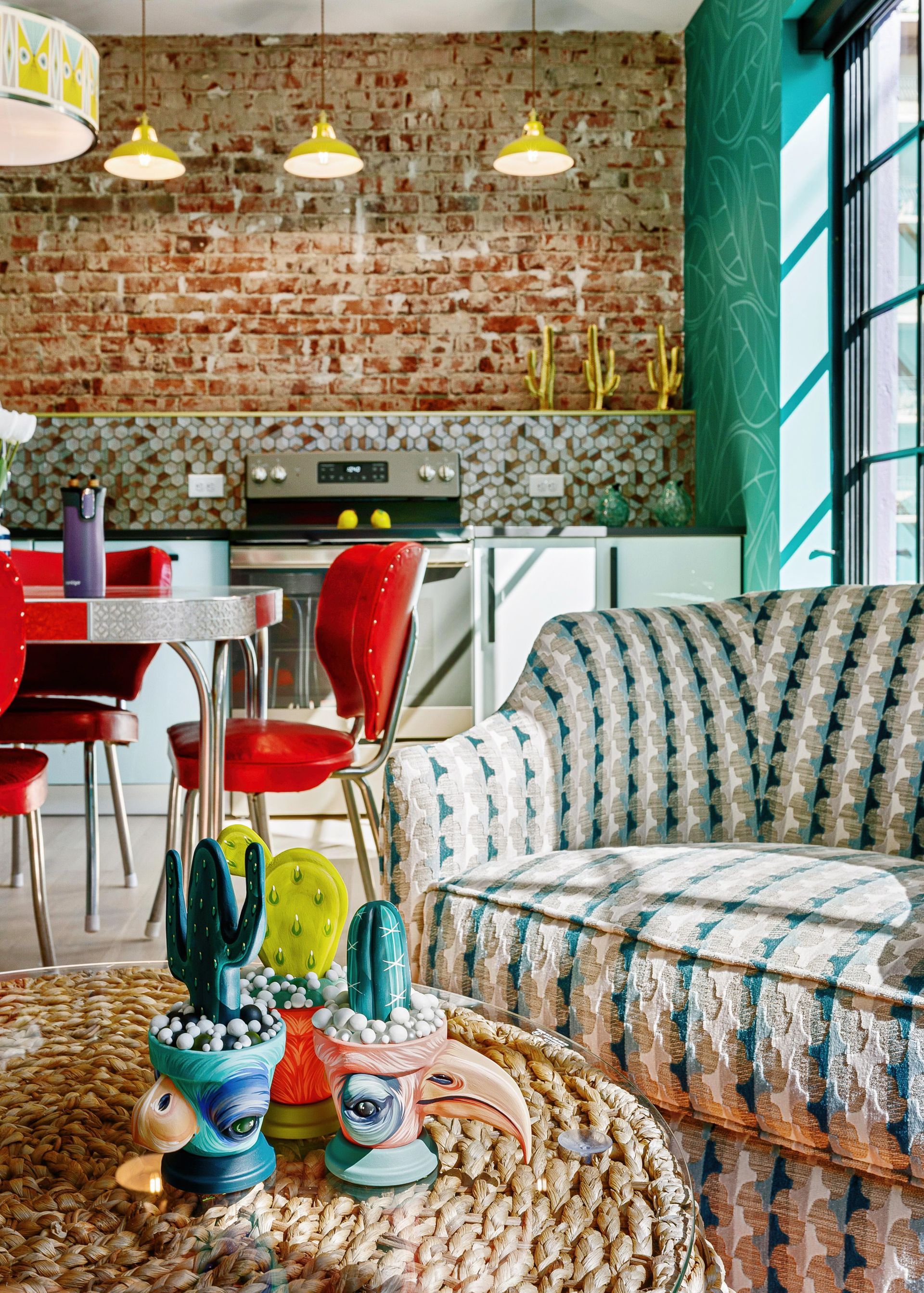 Cozy eclectic living room with patterned sofa, colorful chairs, brick wall, and large windows
