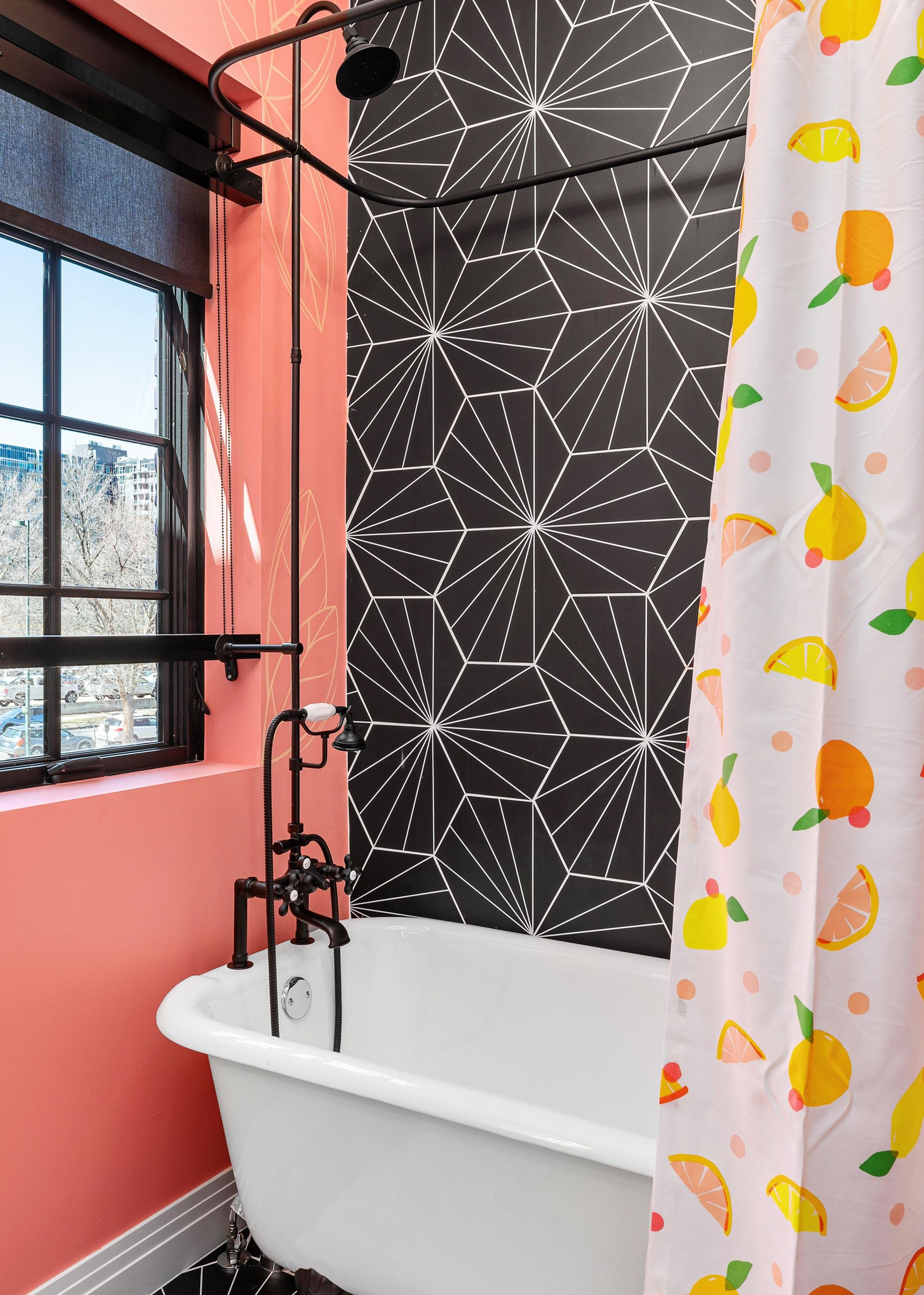 Bright bathroom with coral walls, clawfoot tub, black patterned tile, and a fruit-print shower curtain.