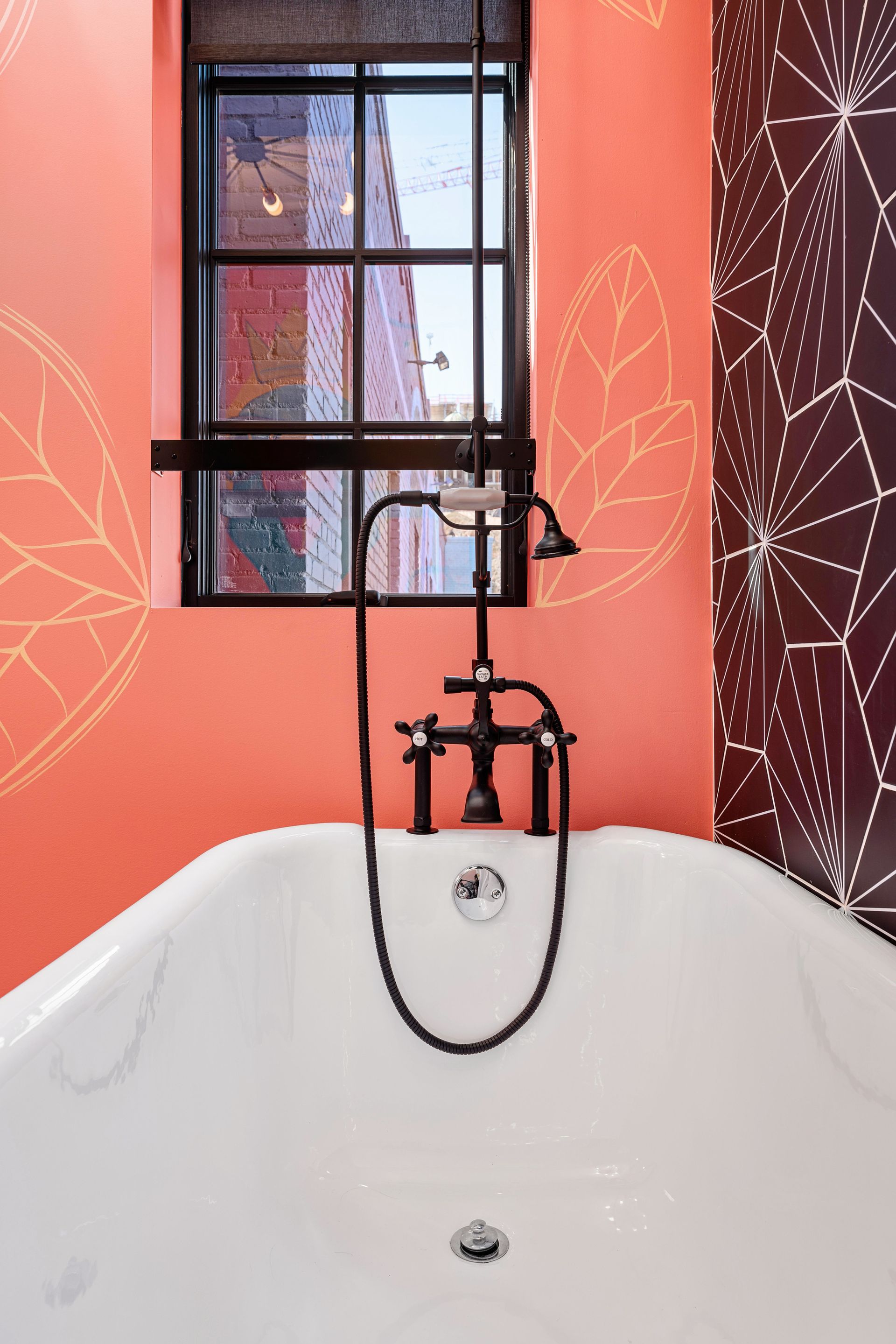 Bathtub with black faucet beneath a window, set against coral and patterned bathroom walls