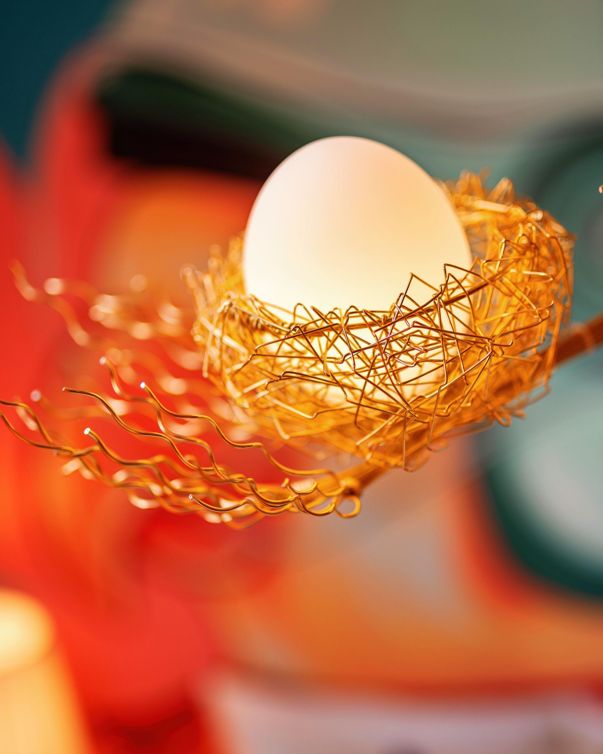 Egg nestled in an orange-gold wire nest on a soft, abstract colorful background