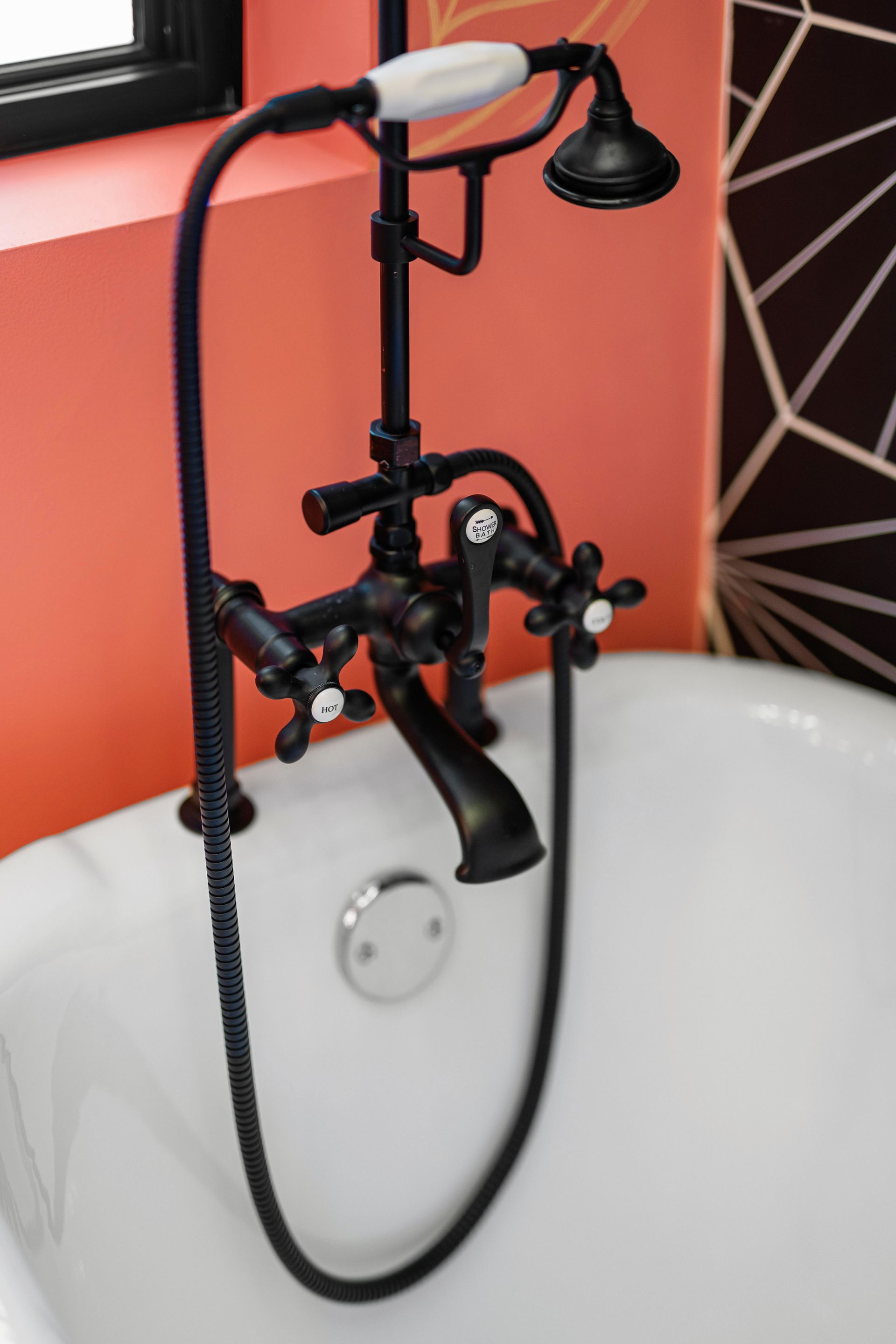 Black vintage-style bathtub faucet with handheld shower over a white sink against a coral wall.