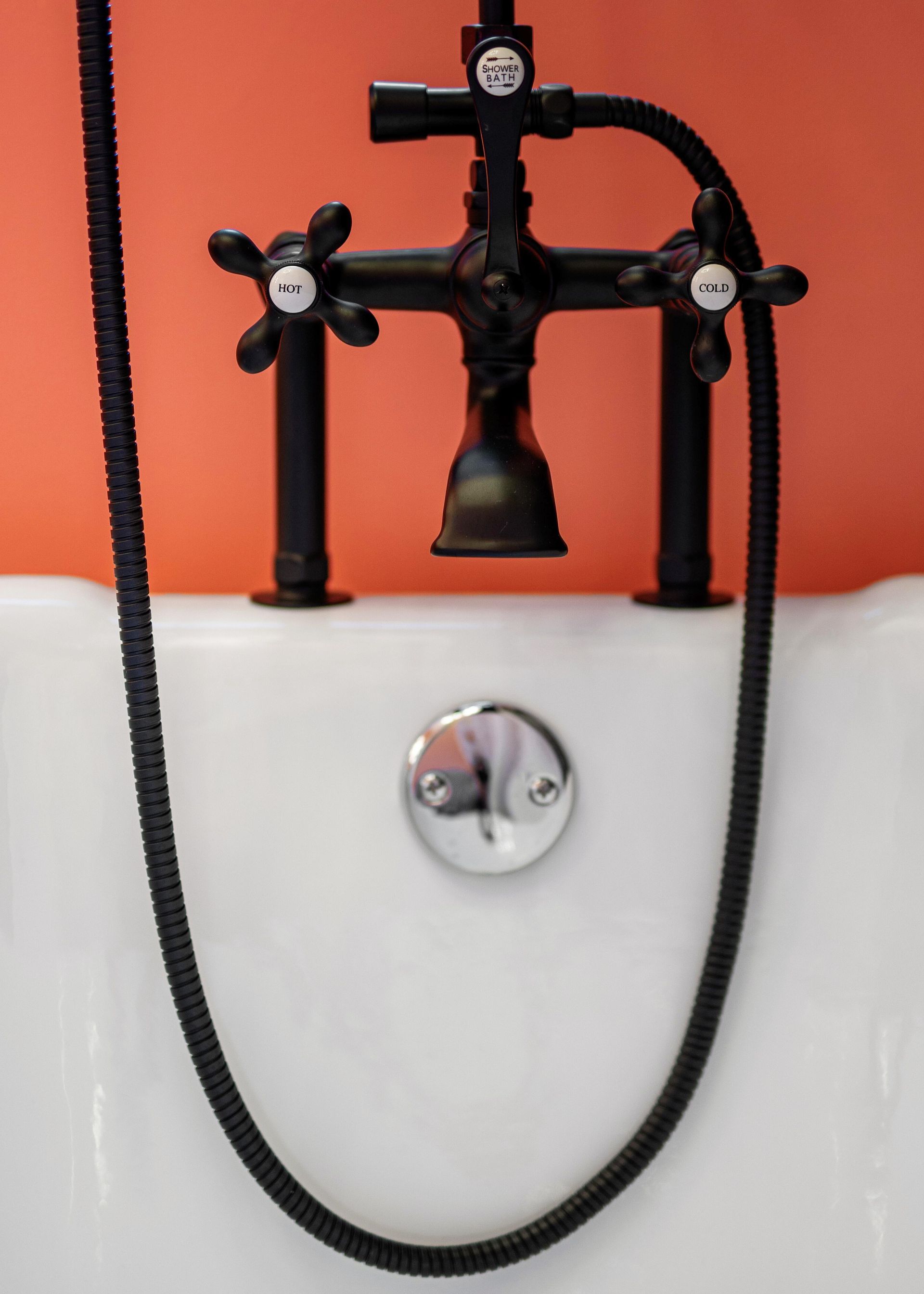 Black faucet with dangling hose on a white sink against an orange wall