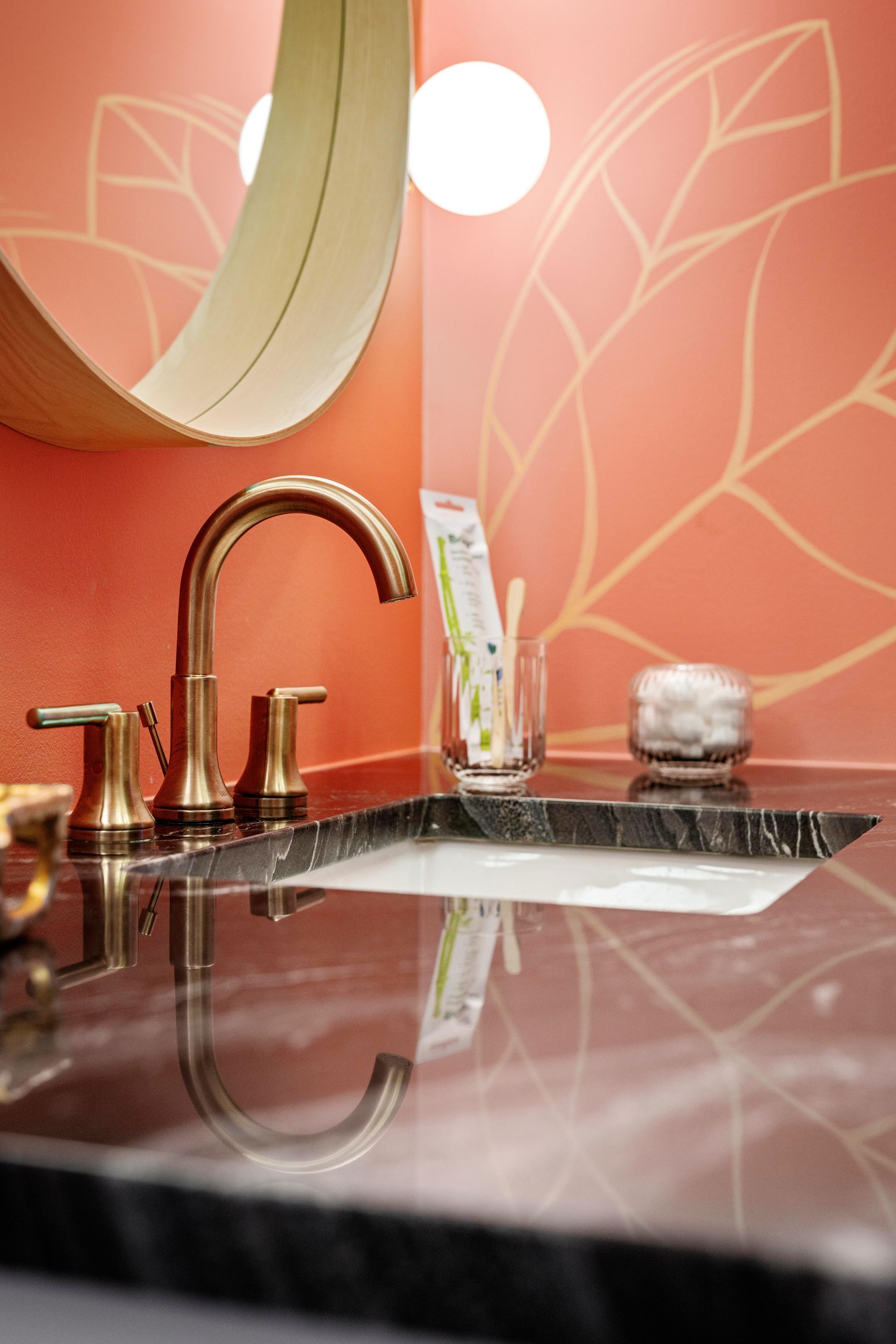 Elegant bathroom vanity with copper faucet, black countertop, and coral floral wallpaper