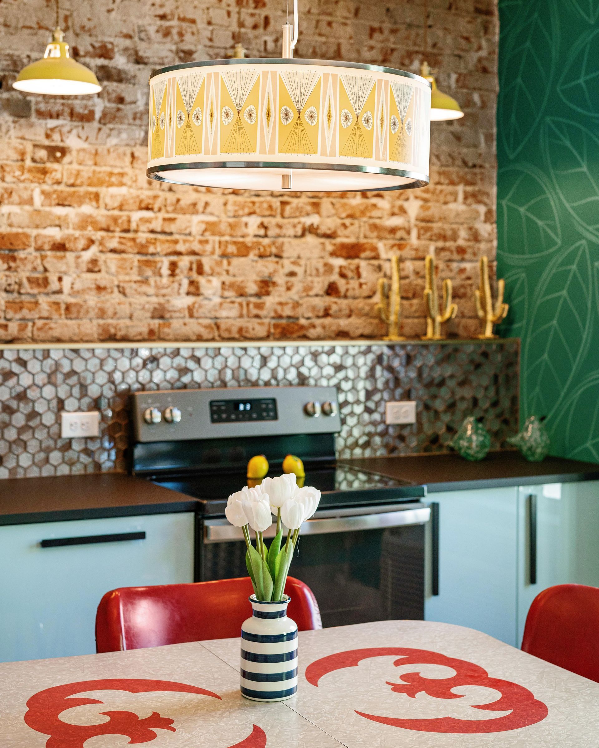 Bright kitchen with brick wall, mint cabinets, stove, and round table with flowers and red placemats