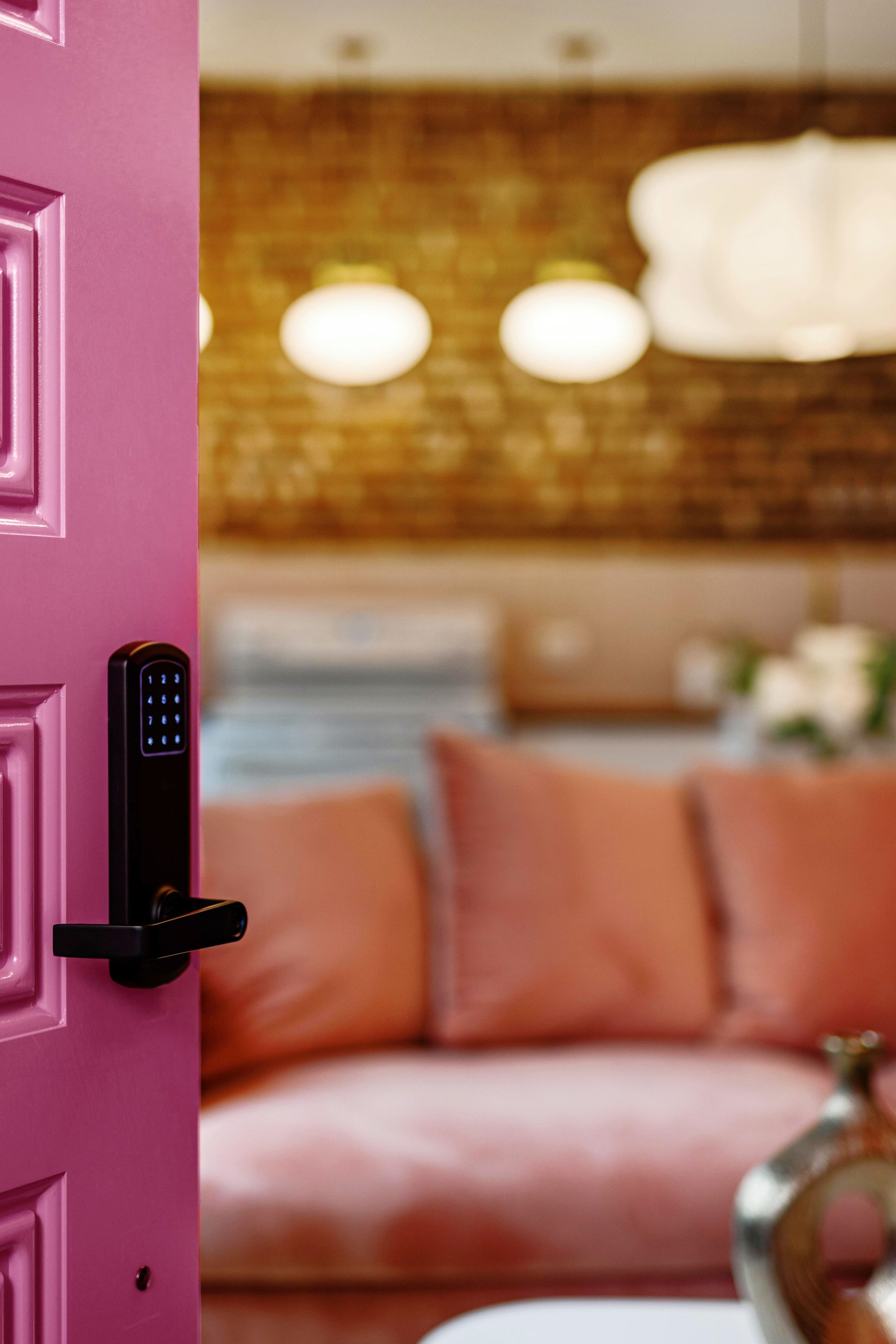 Open pink front door revealing a cozy living room with peach sofa and warm pendant lights
