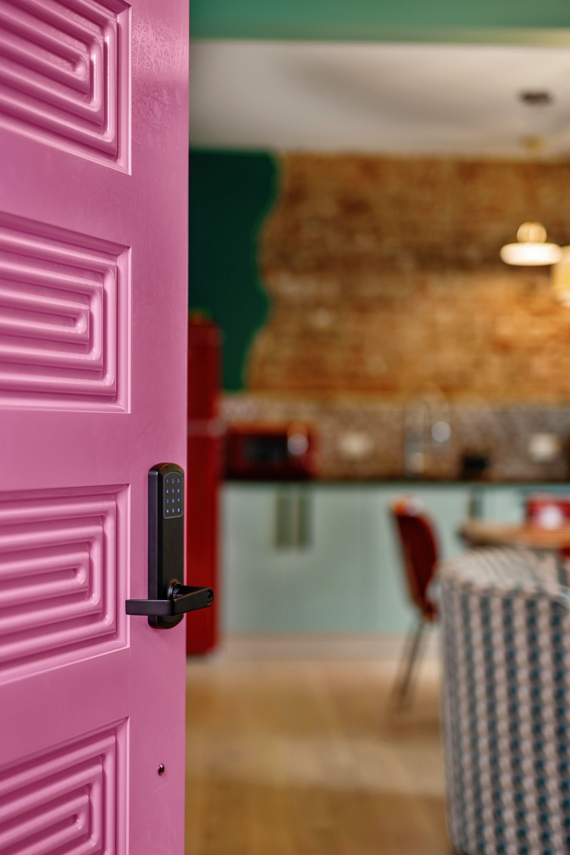 Pink door opens into a cozy restaurant with a blurred dining area and exposed brick wall.