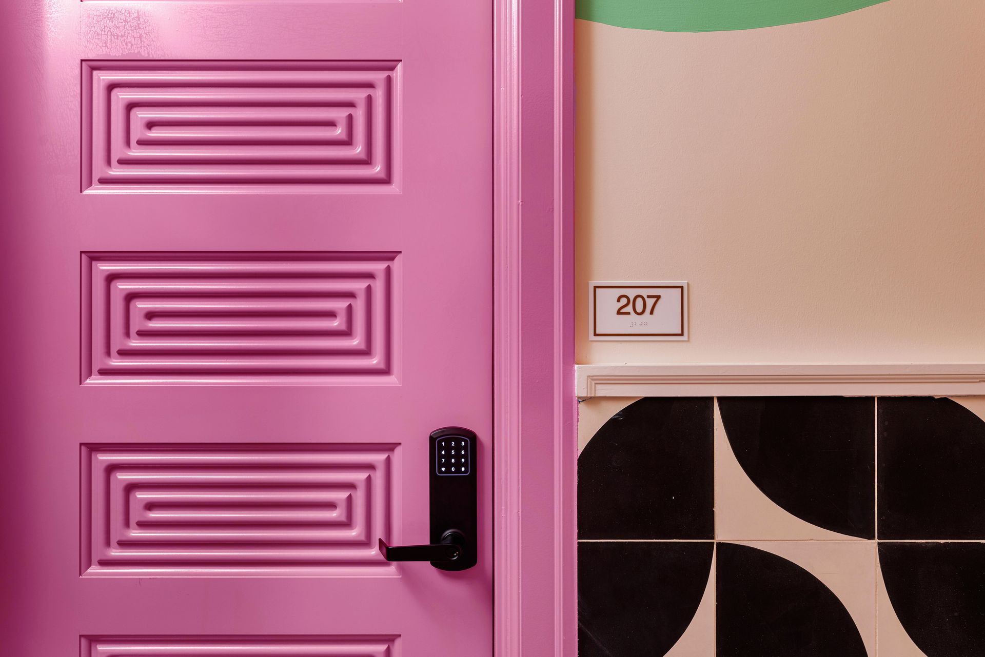 Pink door with black handle next to a beige wall and tiled lower wall, room number 207 above the doorway