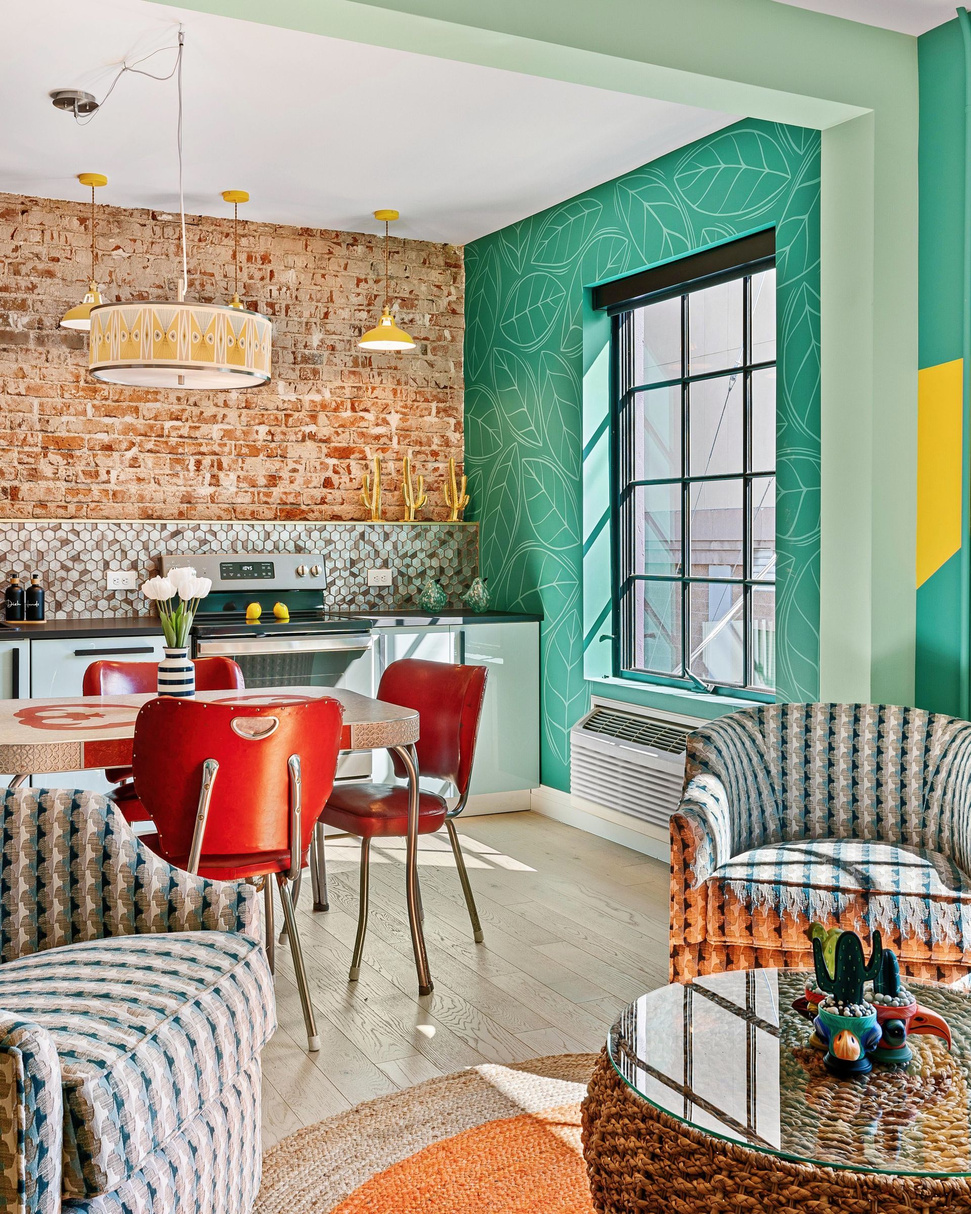 Colorful modern dining room with red chairs, brick wall, teal accents, and patterned armchairs.
