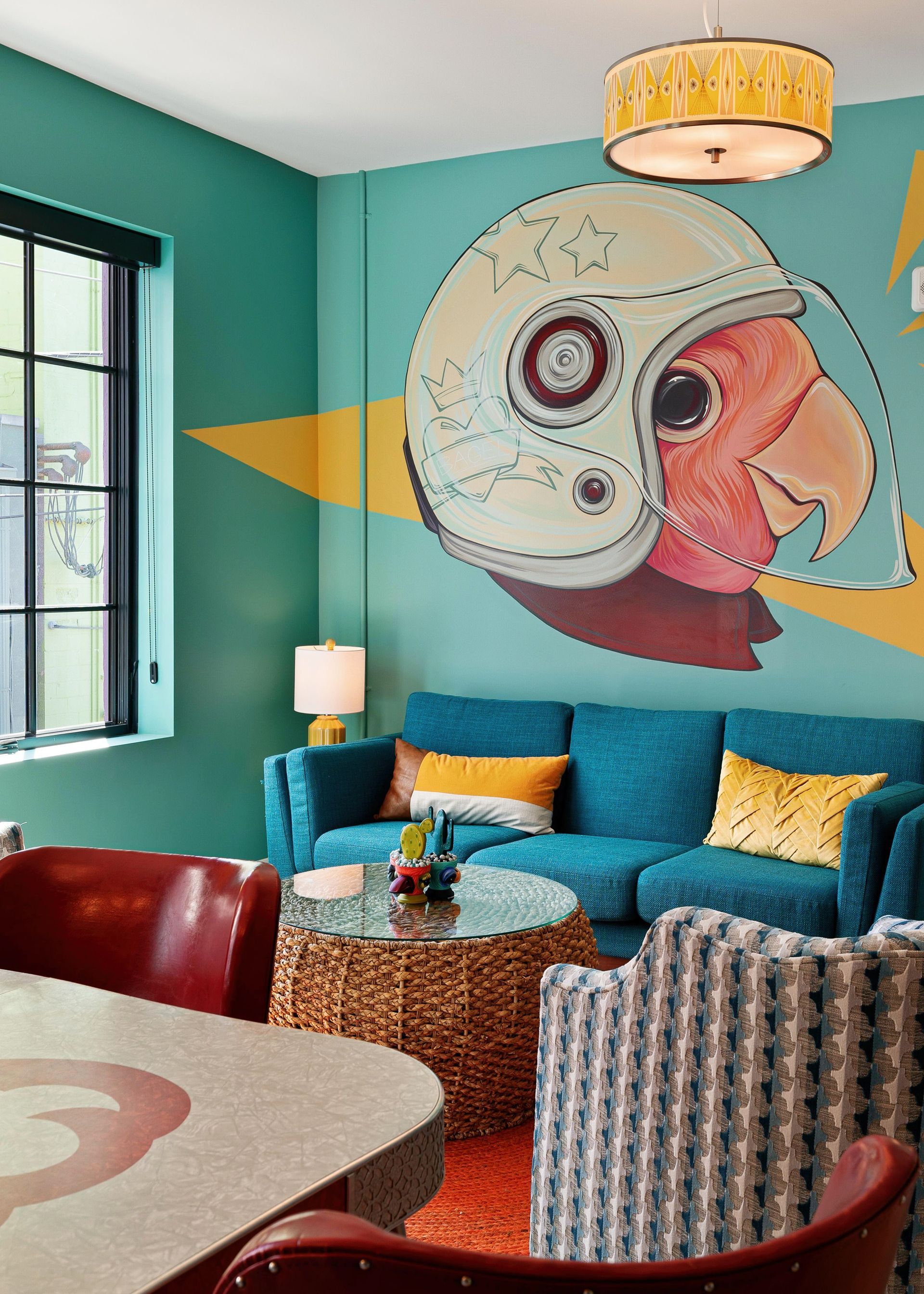 Colorful café corner with teal walls, mural art, blue sofa, red chairs, and a window letting in daylight