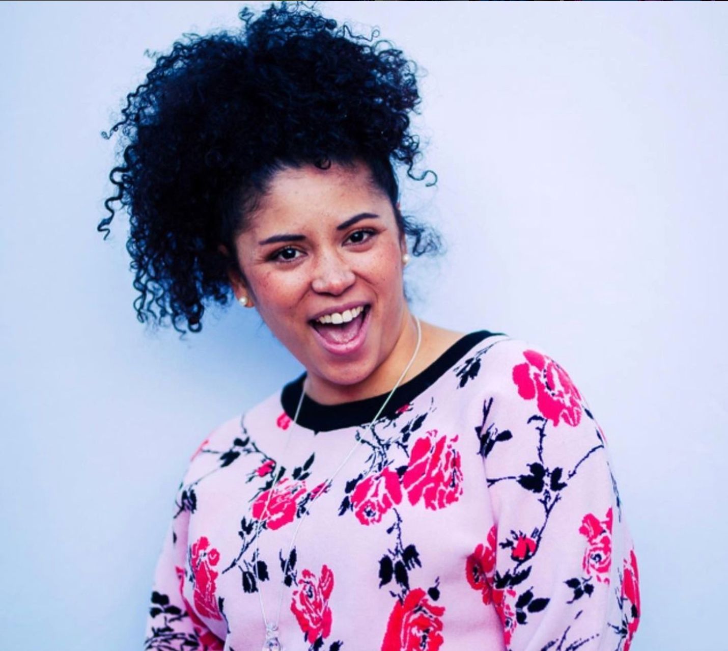 Woman smiling in a white floral top against a light blue background