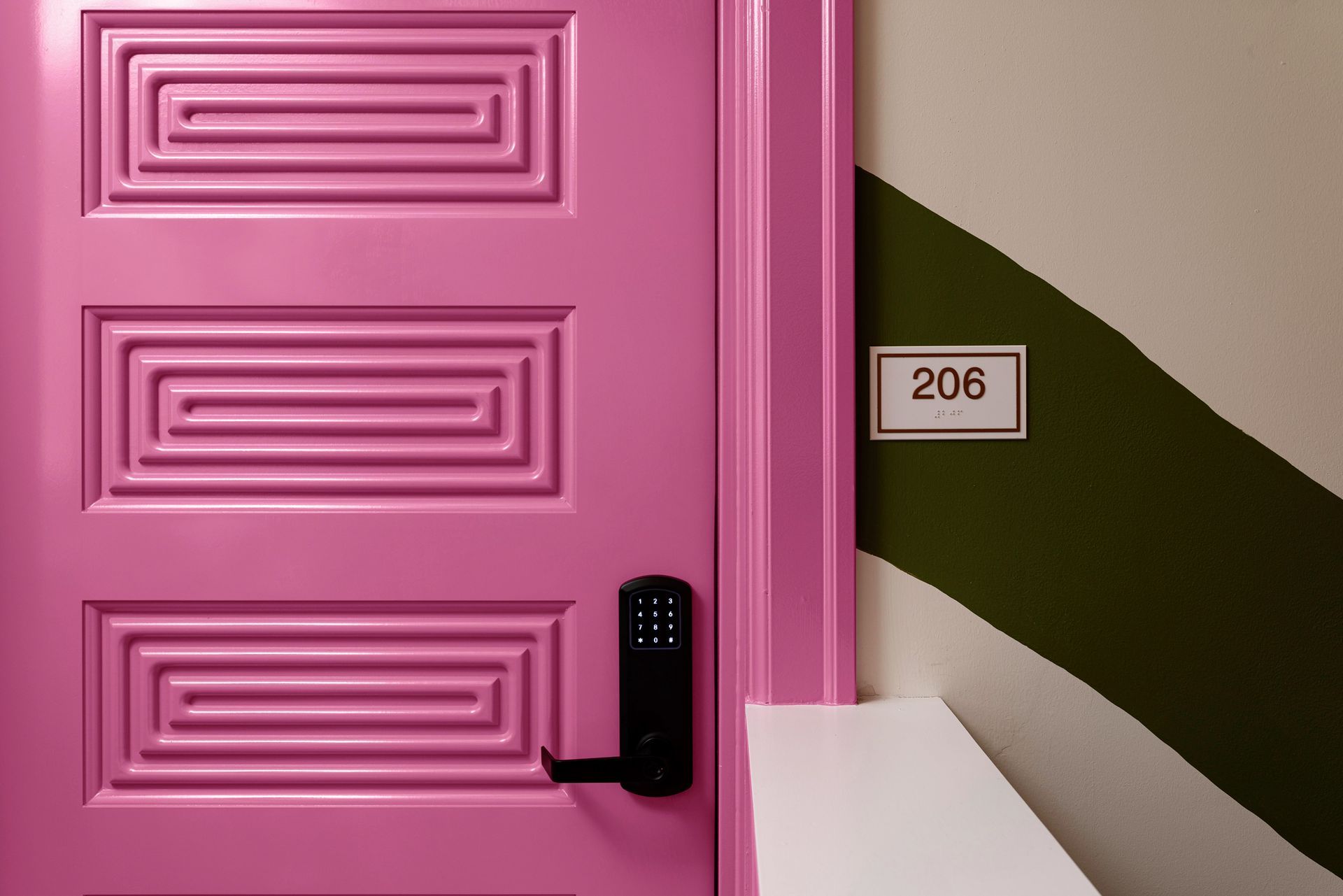 Pink door with black handle and room number 206 beside it, next to a green-and-white wall.