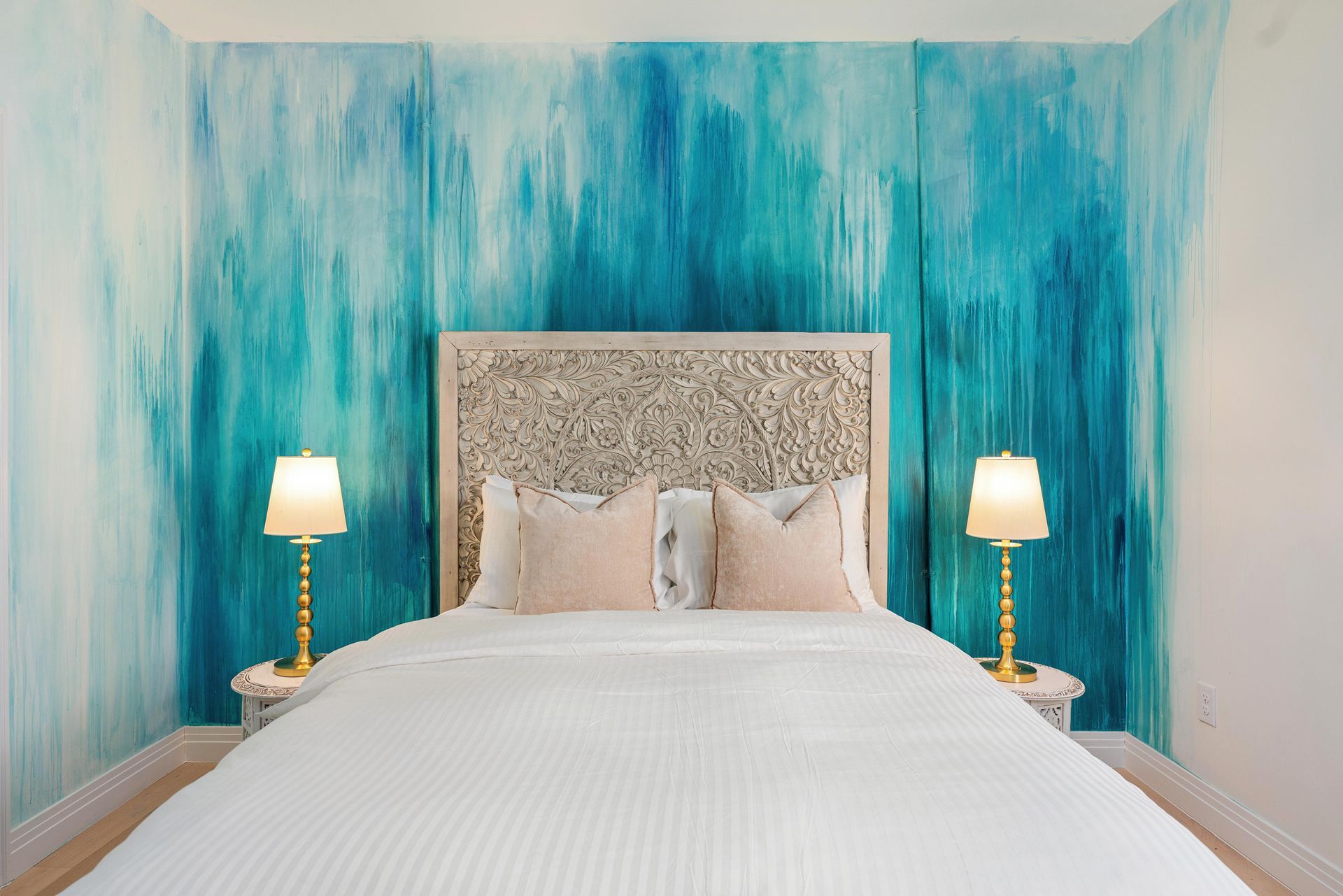 Bright bedroom with a white bed, ornate headboard, and turquoise textured walls, flanked by two lamps