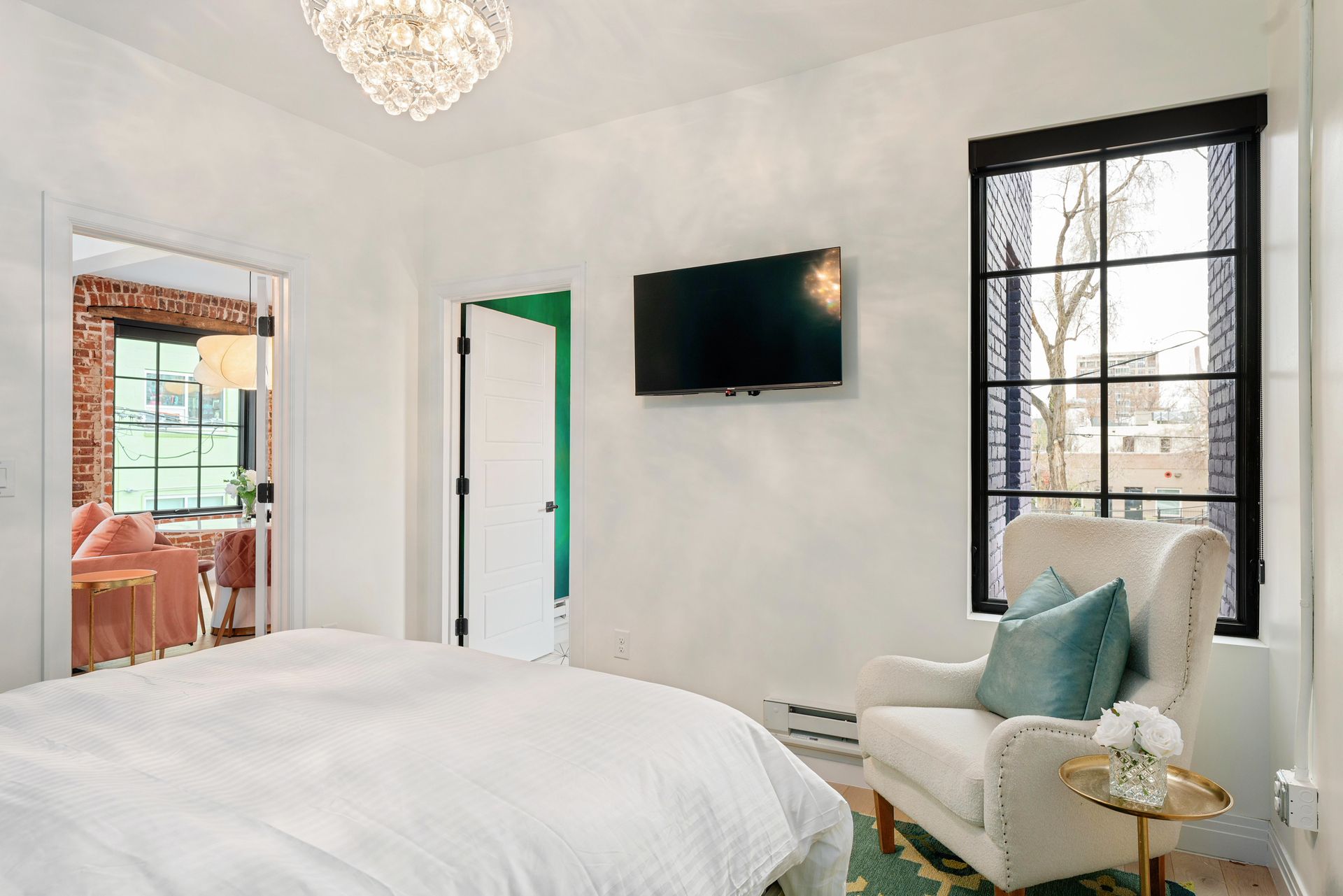 Bright bedroom with white bed, wall-mounted TV, window, and a cozy chair by the corner.