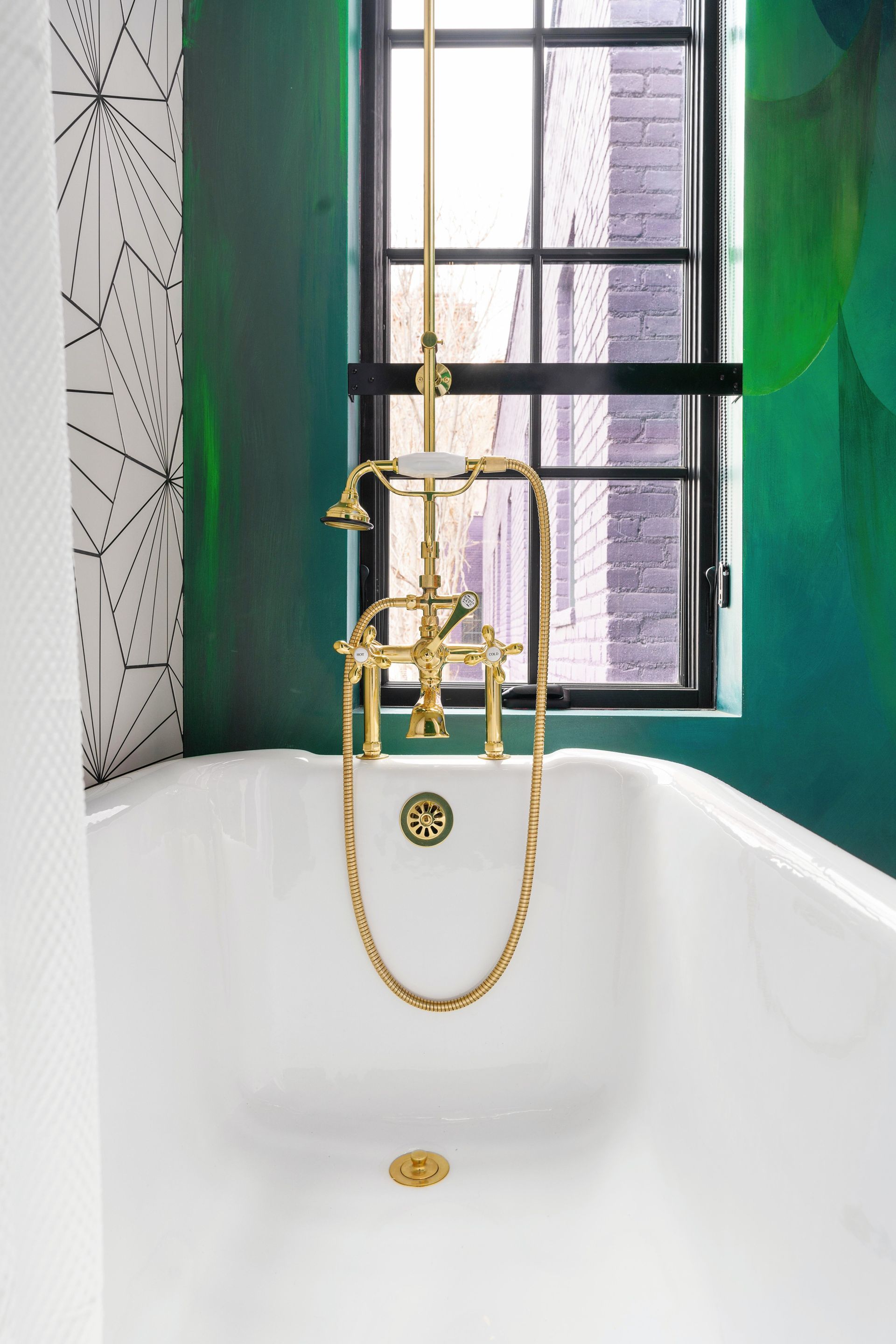 Gold clawfoot bathtub with faucet in a bathroom, set against teal walls and a window.