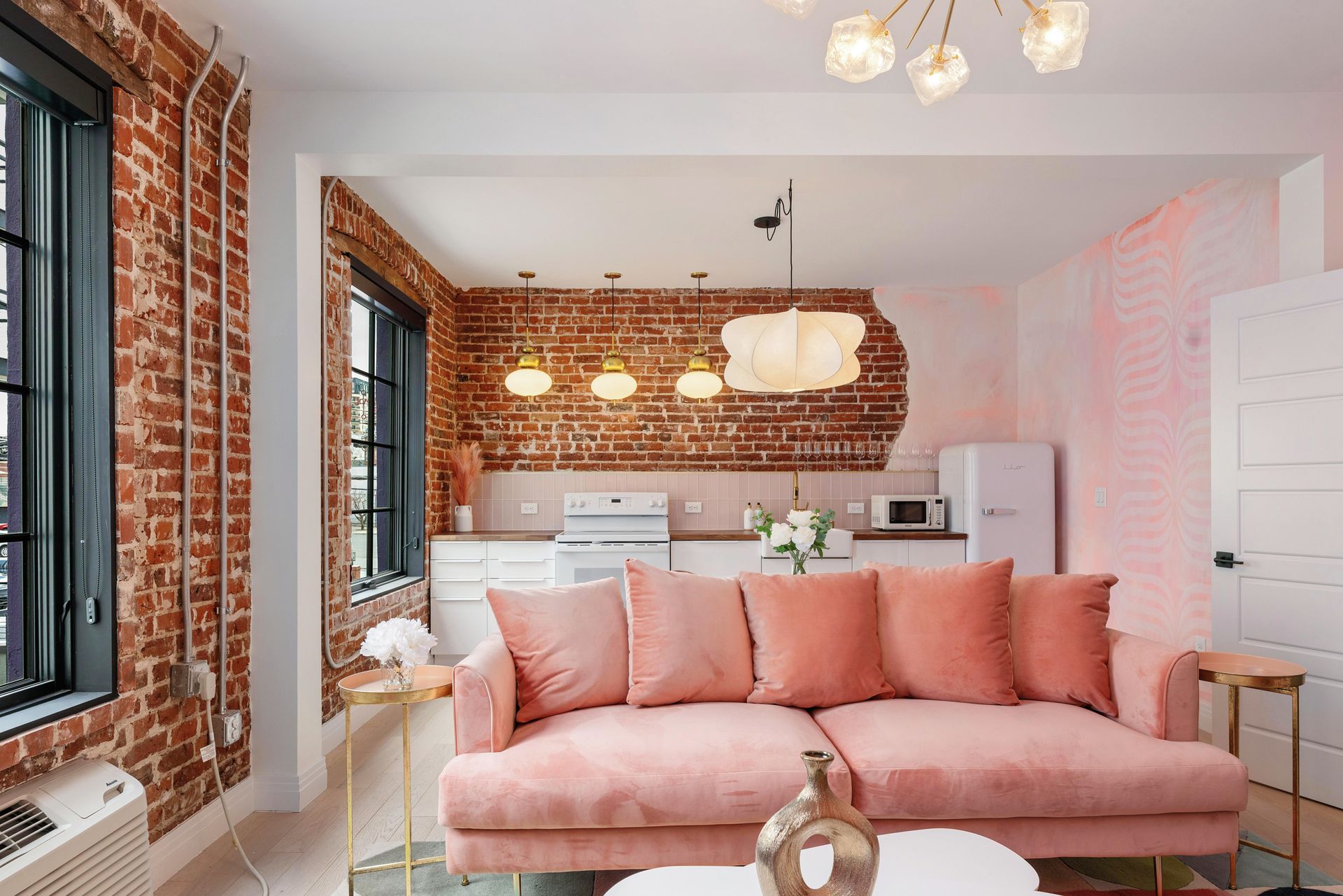 Pink sofa in a bright loft living room with exposed brick and modern kitchen beyond