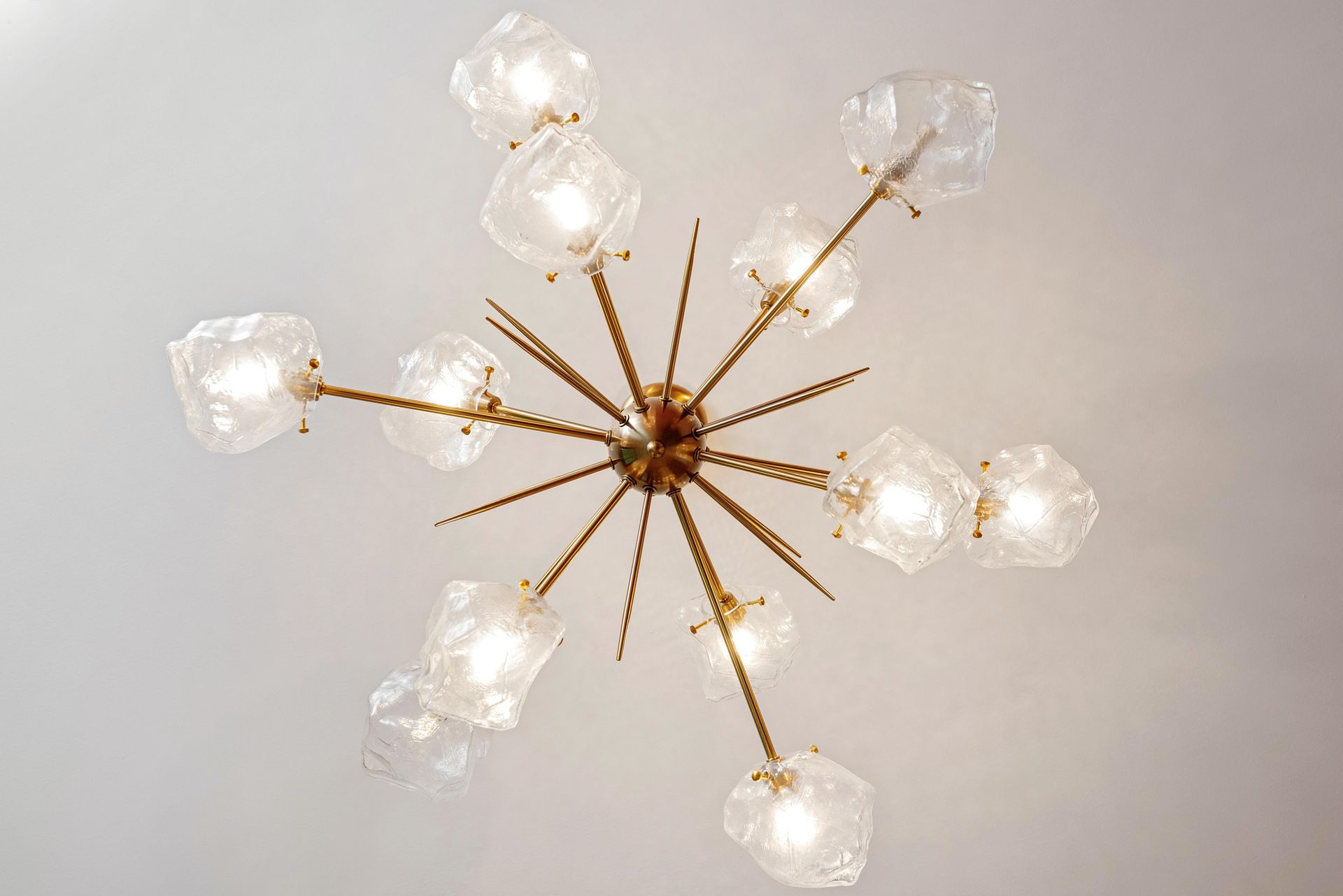 Modern gold chandelier with six frosted glass light shades on a light ceiling