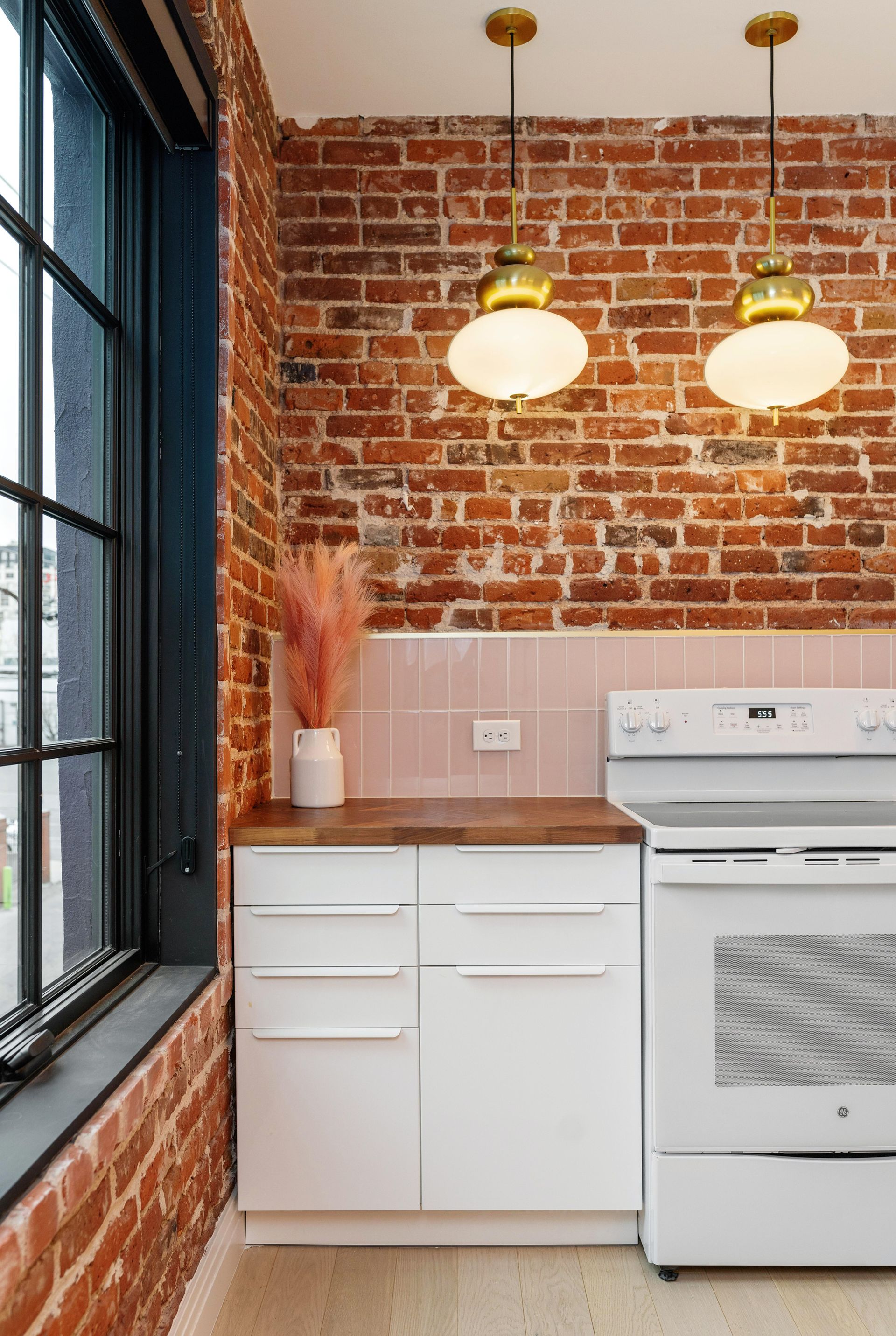 Brick kitchen with white cabinets, wooden counter, pendant lights, and a white stove beside a black-framed window