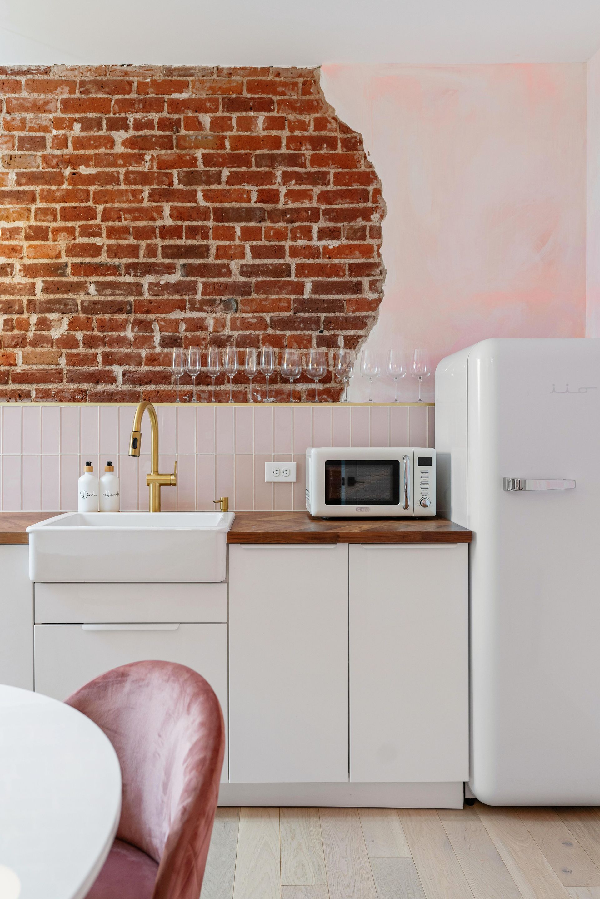 Small kitchen with exposed brick wall, white cabinets, sink, microwave, and fridge.