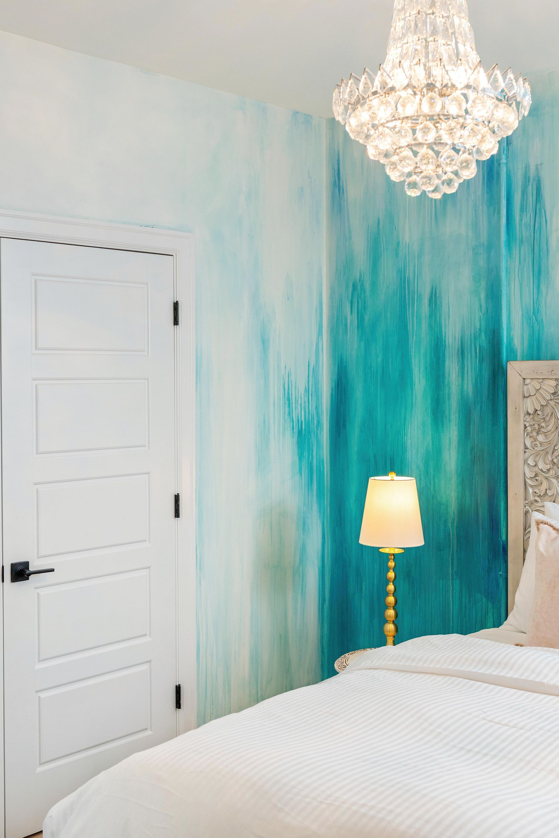 Bright bedroom with turquoise accent wall, white bed, chandelier, and closed door