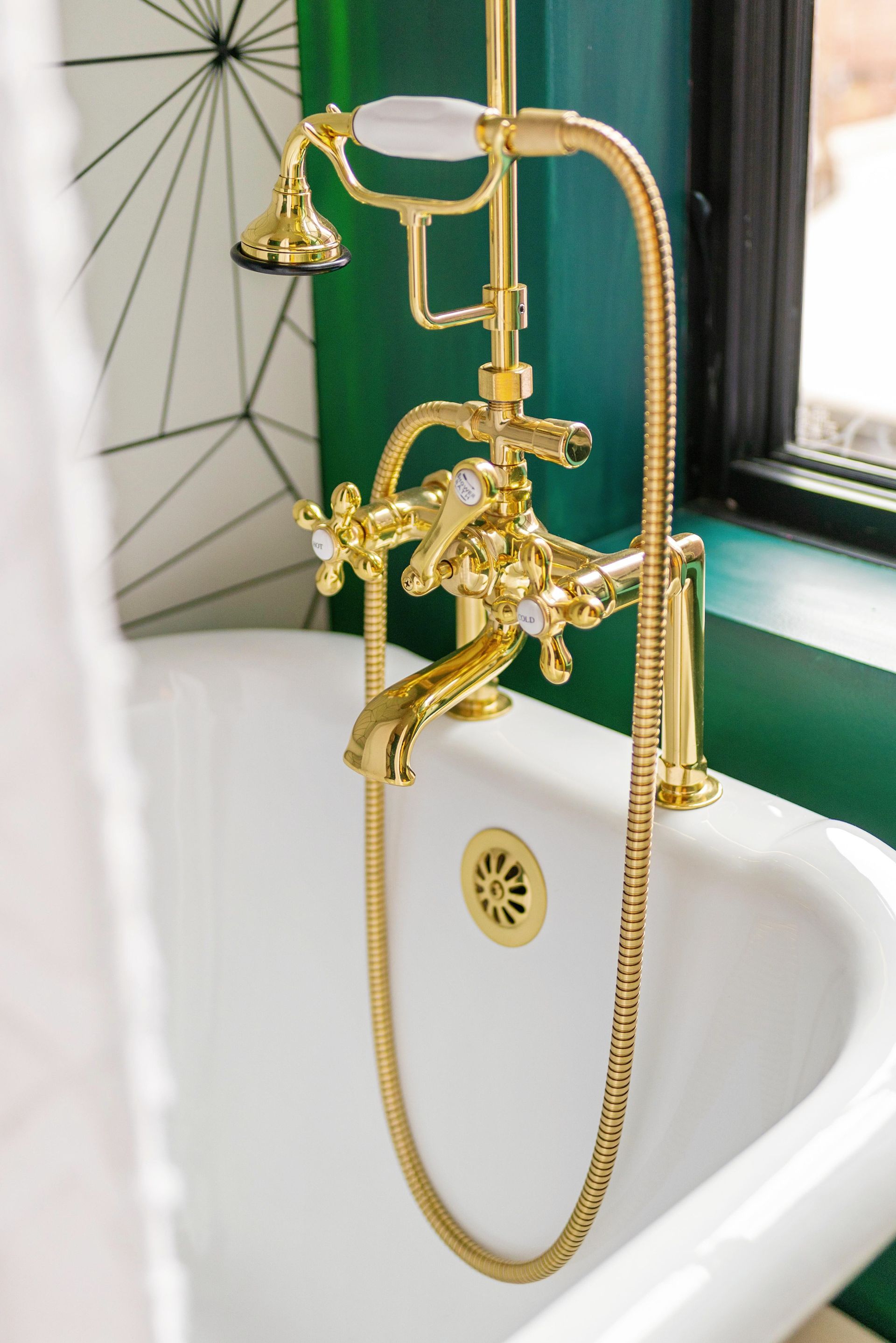 Gold clawfoot bathtub faucet with handheld shower and chain in a white tub by a green wall