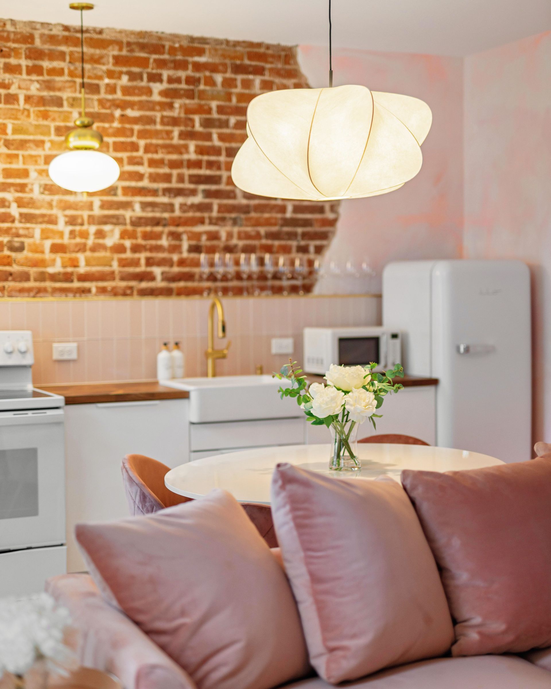 Cozy kitchen with pink sofa, exposed brick wall, white fridge, and pendant lights