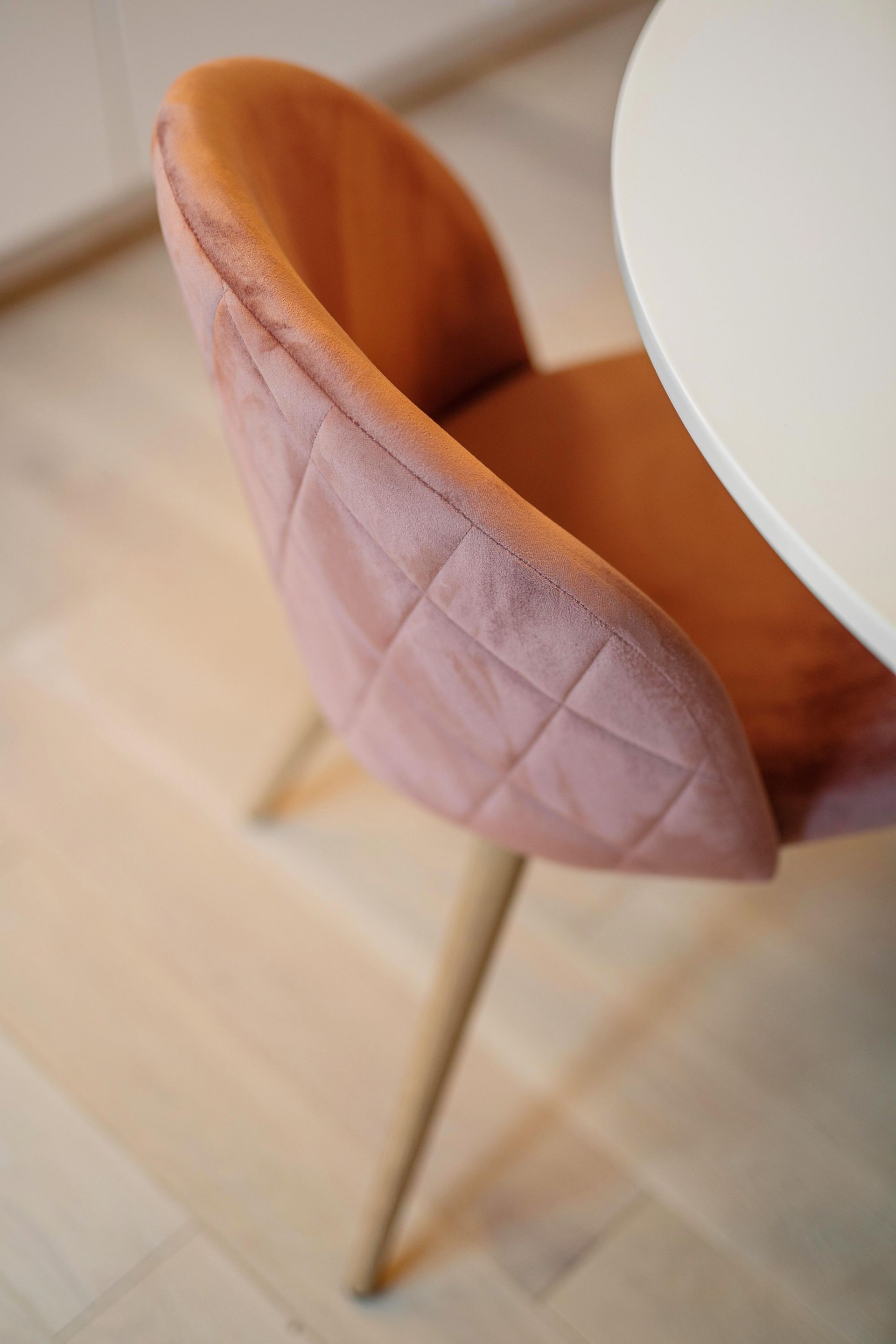Pink quilted dining chair beside a white table on a light wood floor