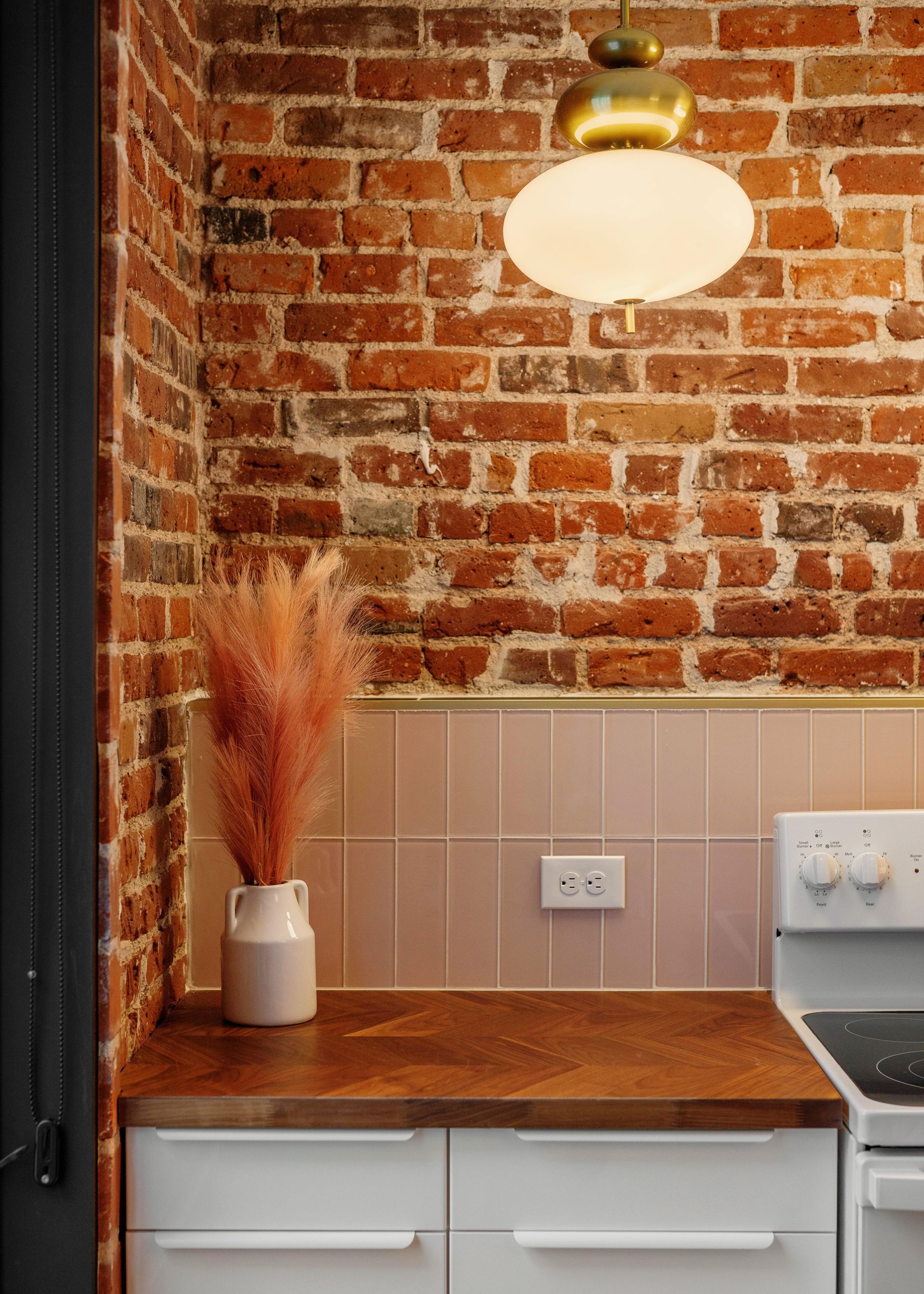 Small kitchen nook with exposed brick wall, wooden counter, white cabinets, and hanging light fixture.