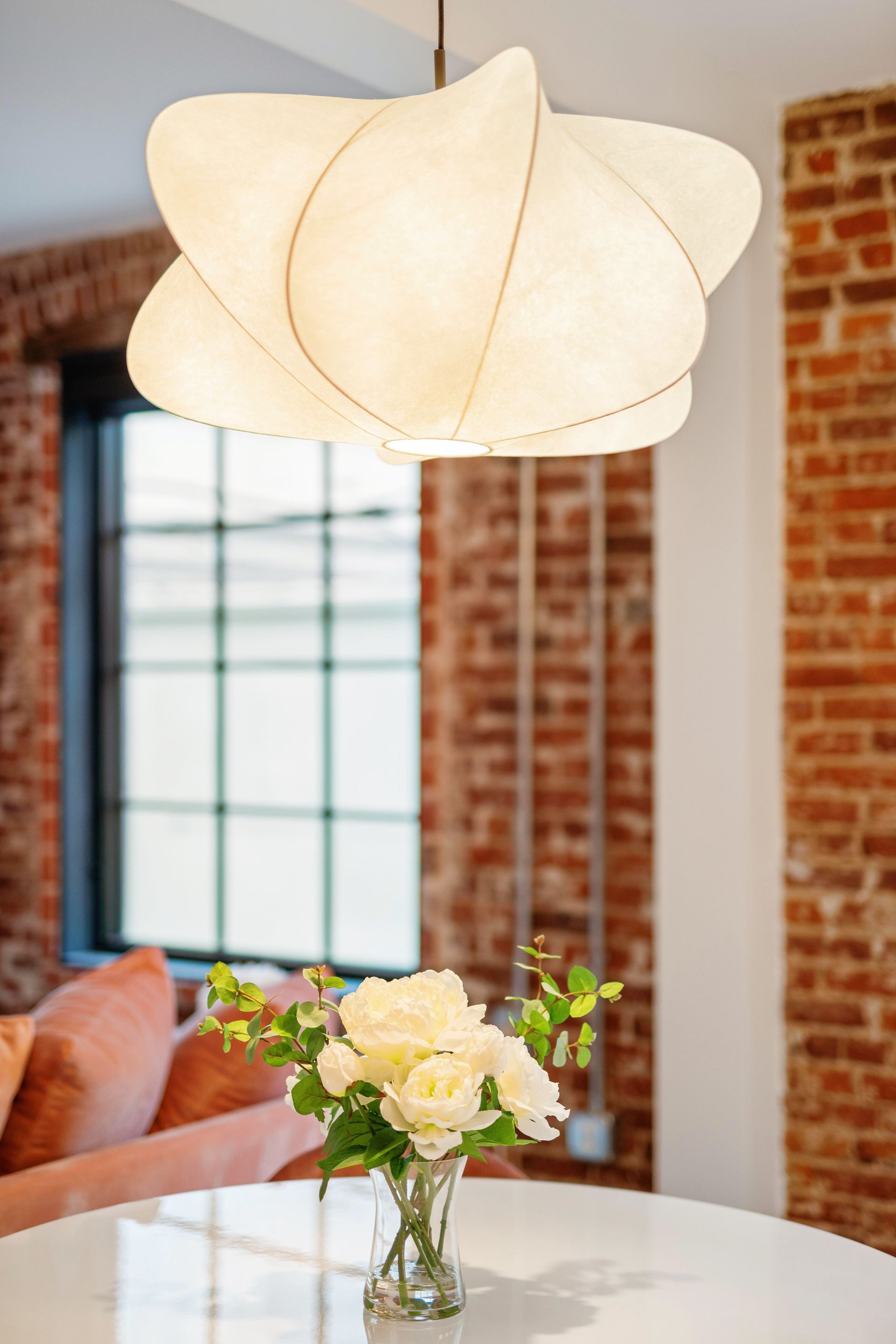 White pendant lamp above a round table with flowers in a cozy brick-walled room