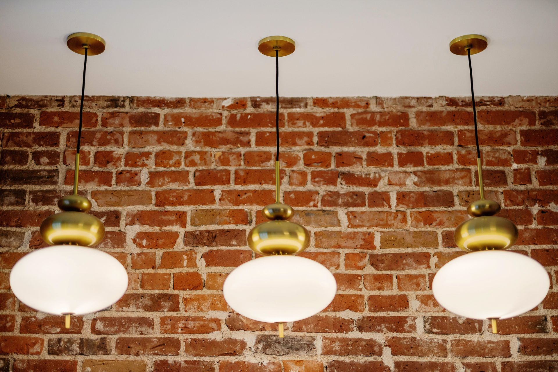 Three brass-and-white pendant lights hanging against a red brick wall.