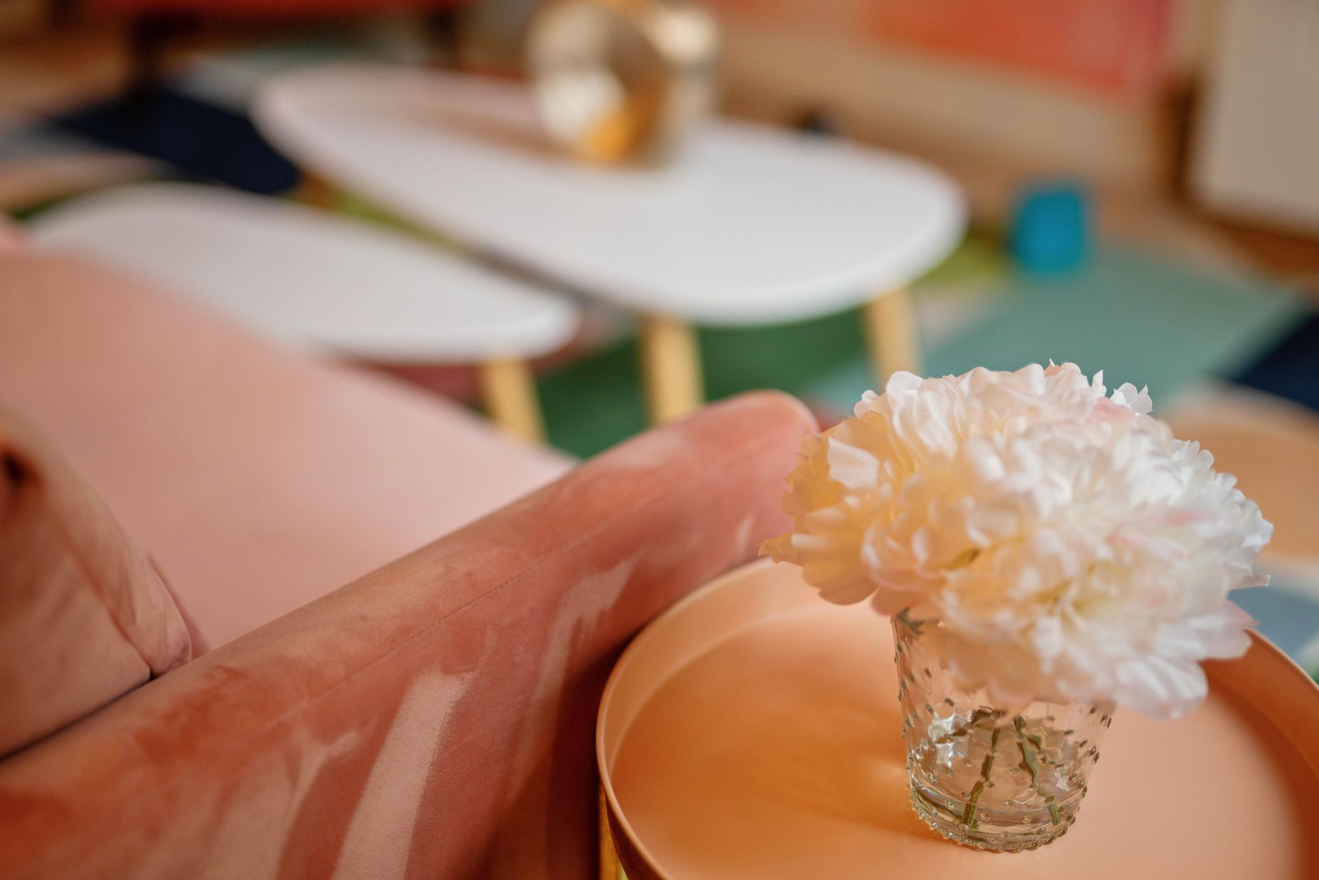 Hand holding a peach bowl with white flowers, beside a blurred vase on a table.
