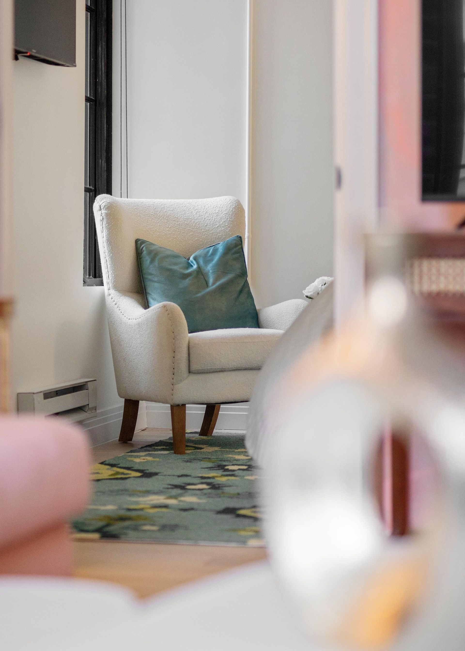 White armchair with teal pillow in a softly lit room, seen through a blurred foreground.
