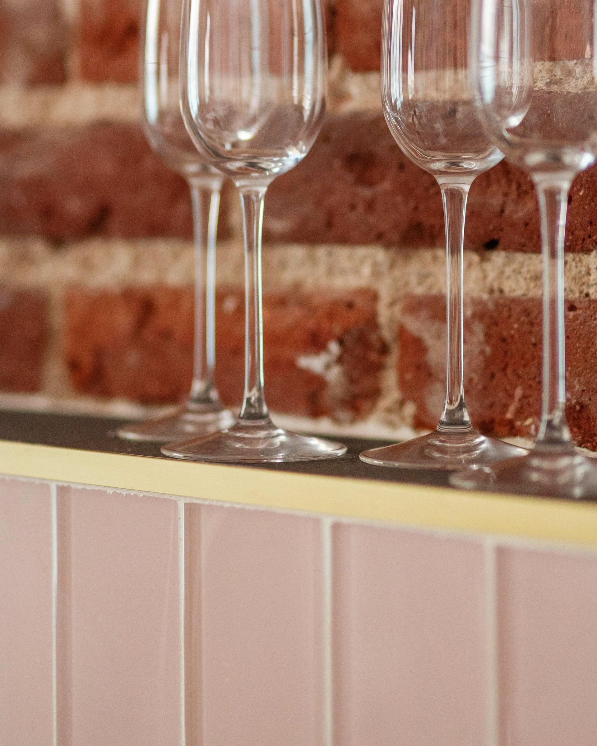 Wine glasses on a counter against a brick wall and pink tiled backsplash