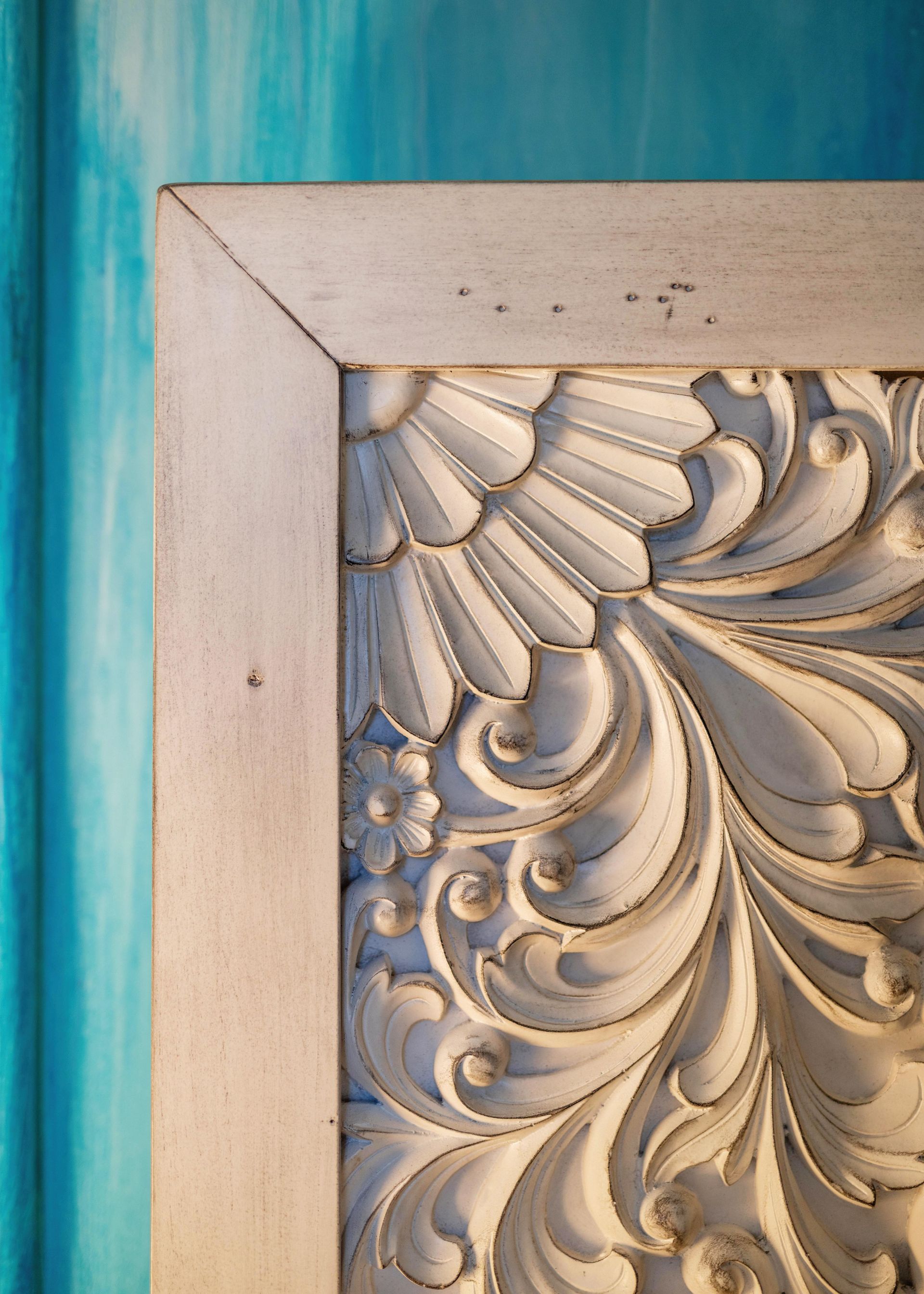 Close-up of an ornate cream carved frame against a blue wall.
