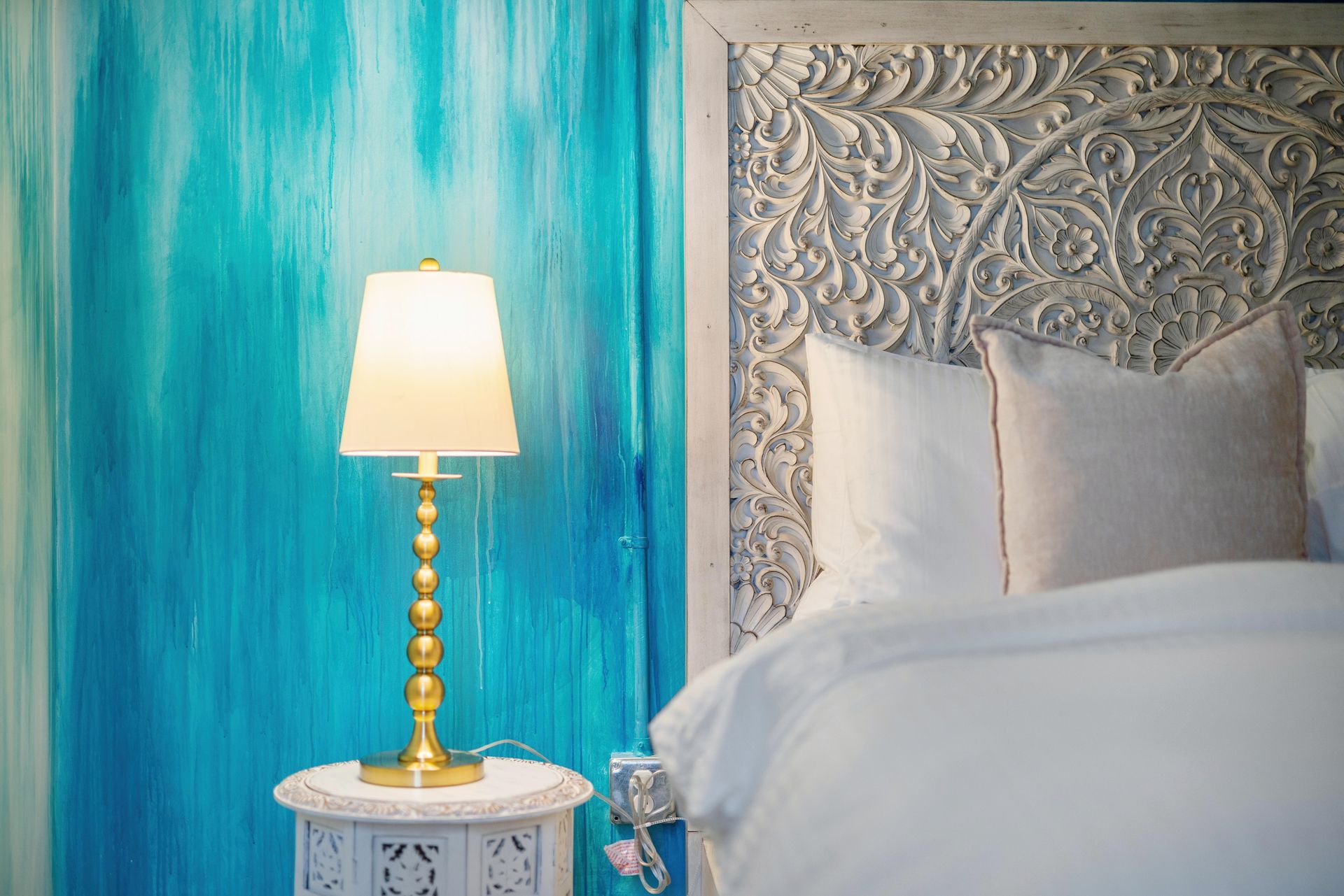Blue bedroom with ornate headboard, white bedding, and a lit gold lamp on a small table
