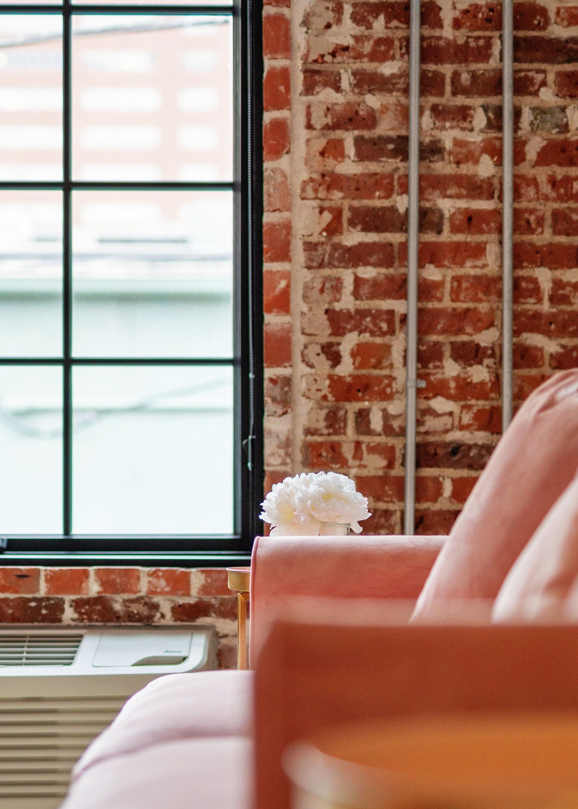 Brick-walled loft interior with a large window and an orange sofa in the foreground