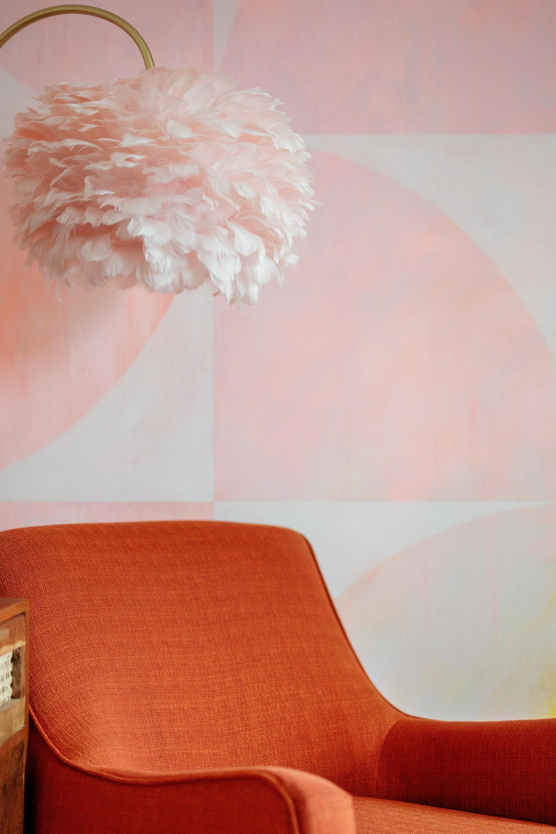 Pink fluffy wall lamp above an orange chair against a pale pink wall.