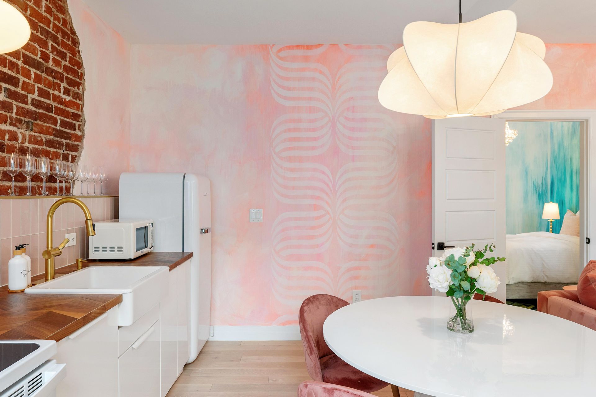 Bright pink kitchen-dining space with white cabinets, round table, and hanging flower-shaped light