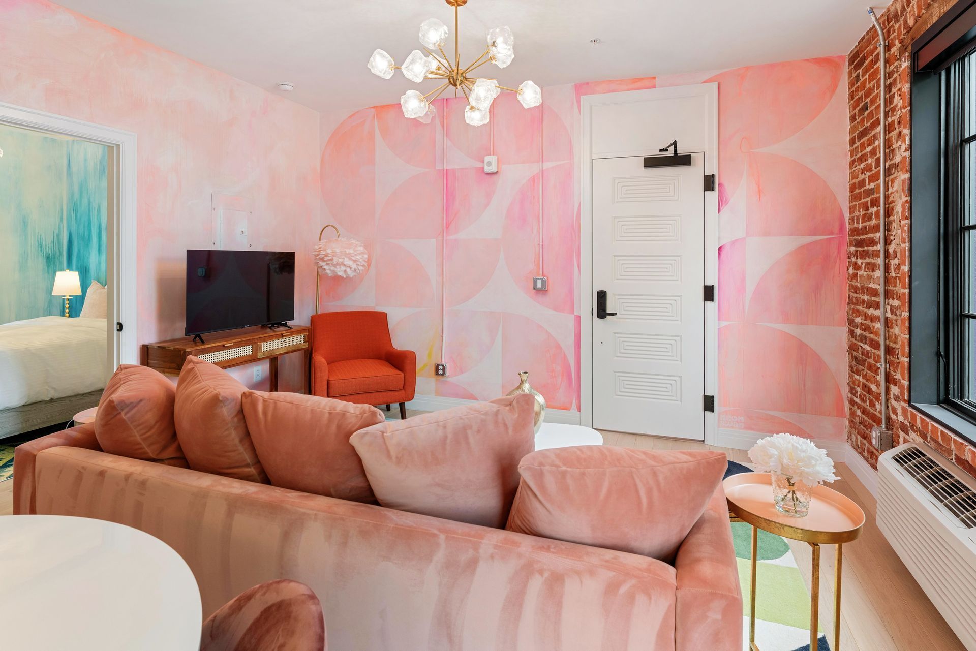Pink living room with a tan sofa, TV, white door, and large window with brick wall accents