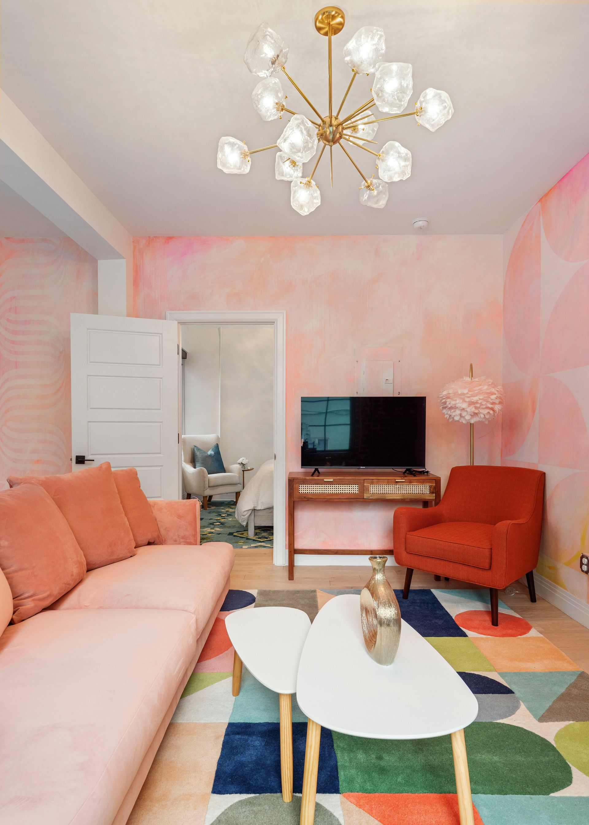 Pastel pink living room with coral sofa, orange chair, TV, and geometric rug